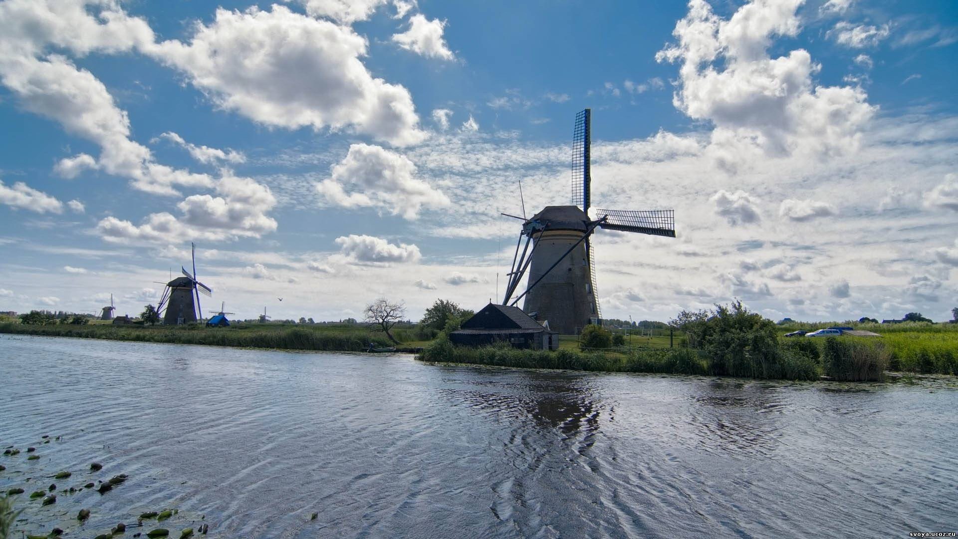 Windmills along a canal under a cloudy sky HD Wallpaper