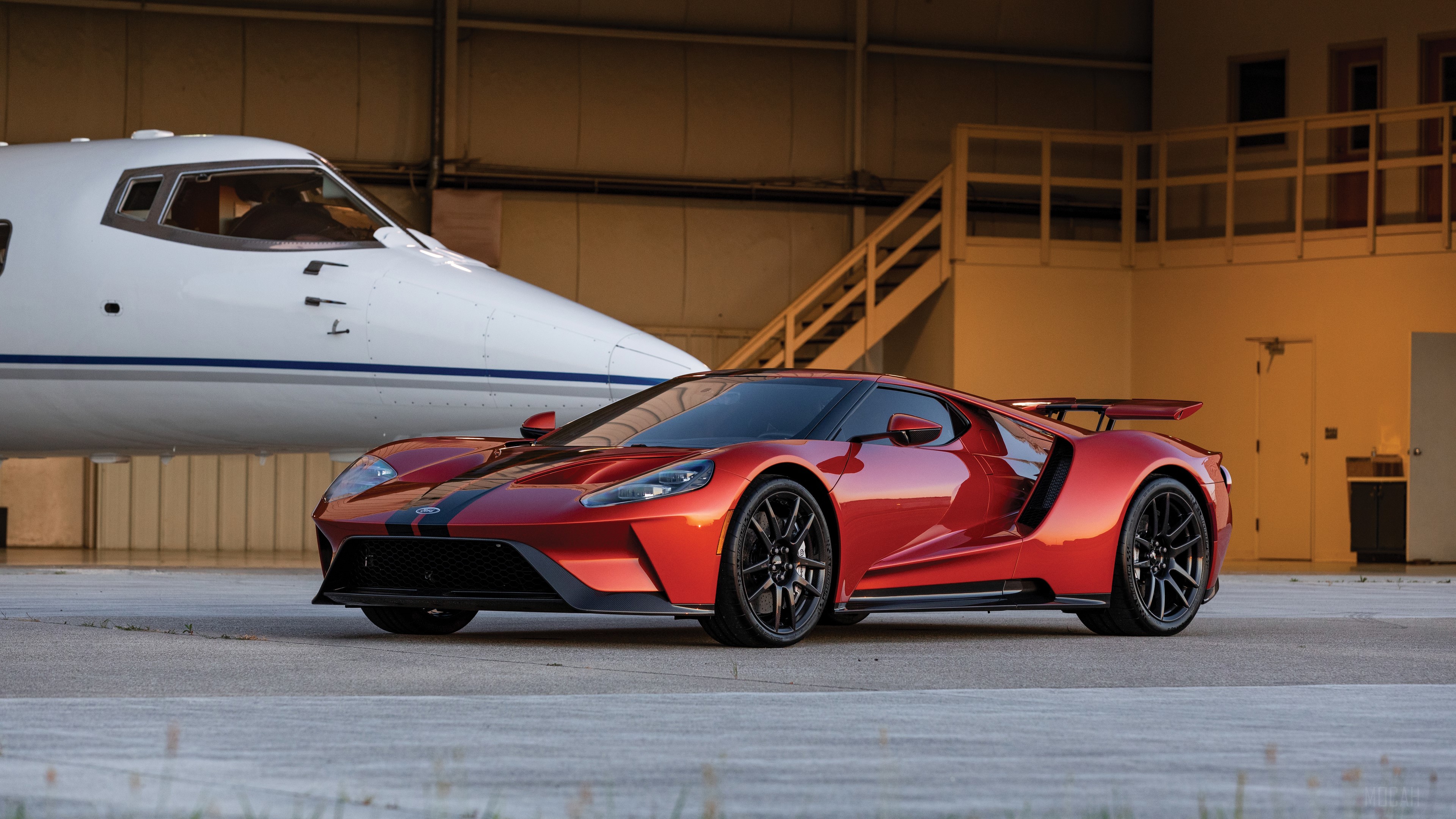 Red Ford GT parked next to a private jet HD Wallpaper