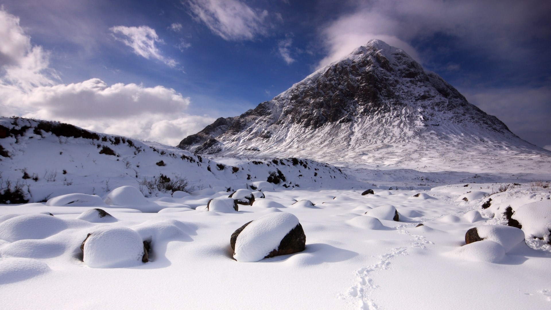 Snowy mountain landscape with rocks and footprints HD Wallpaper