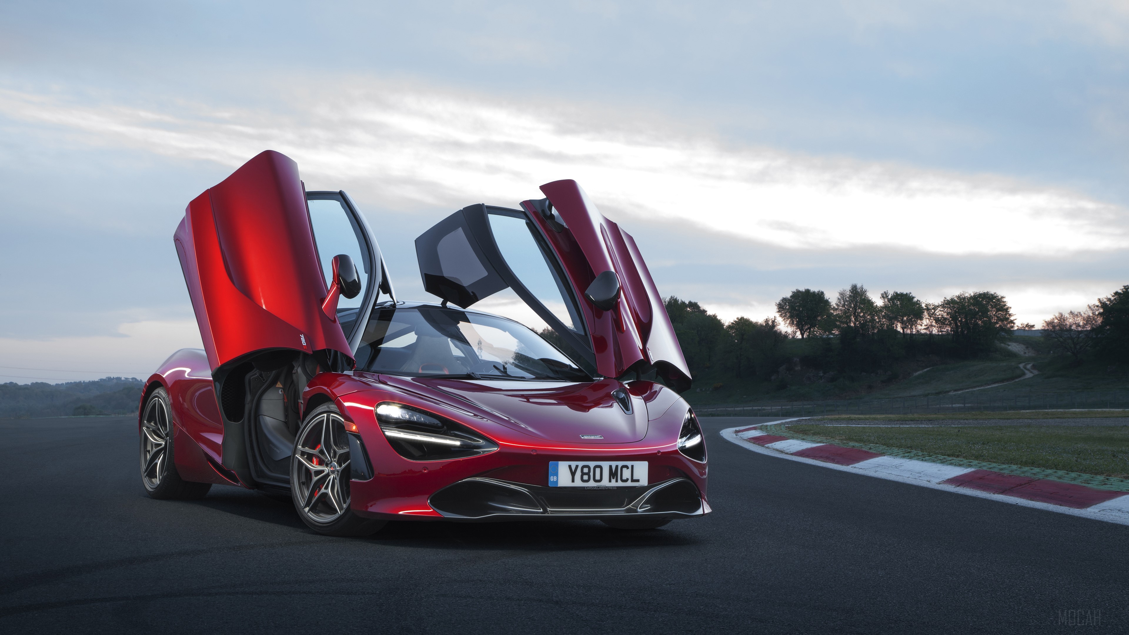Red McLaren 720S with doors open on a racetrack HD Wallpaper