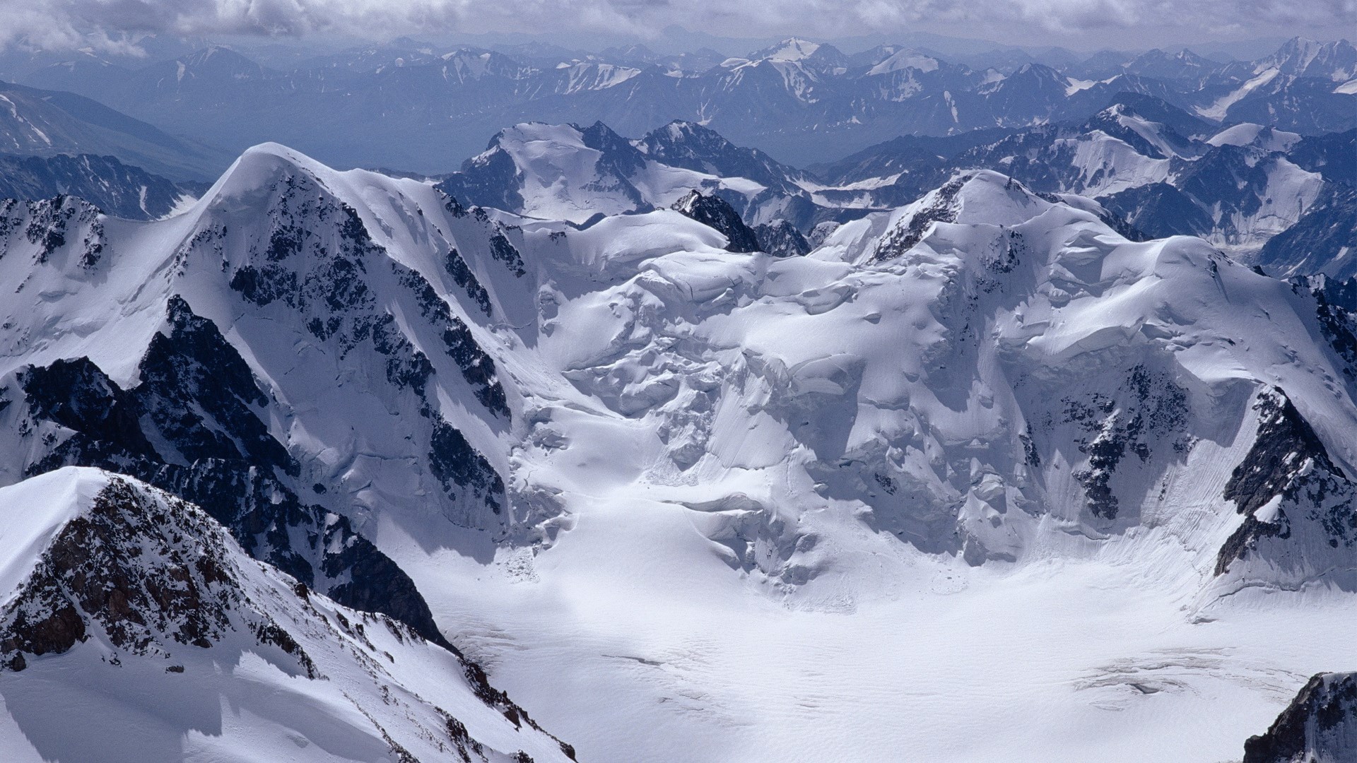 Snow-covered mountain range under a cloudy sky HD Wallpaper