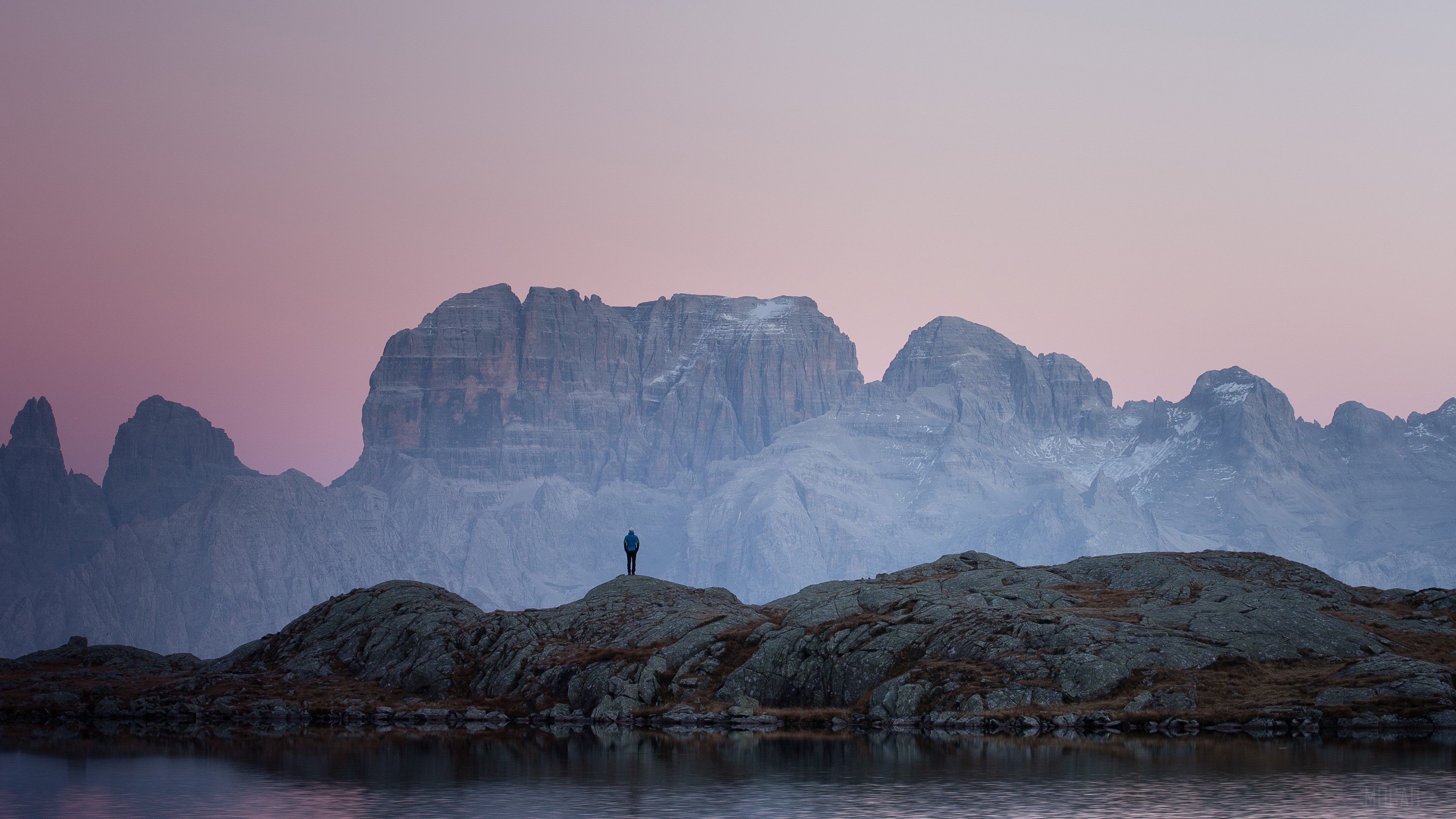 Person standing on rocks overlooking mountains at sunset 4K HD Wallpaper