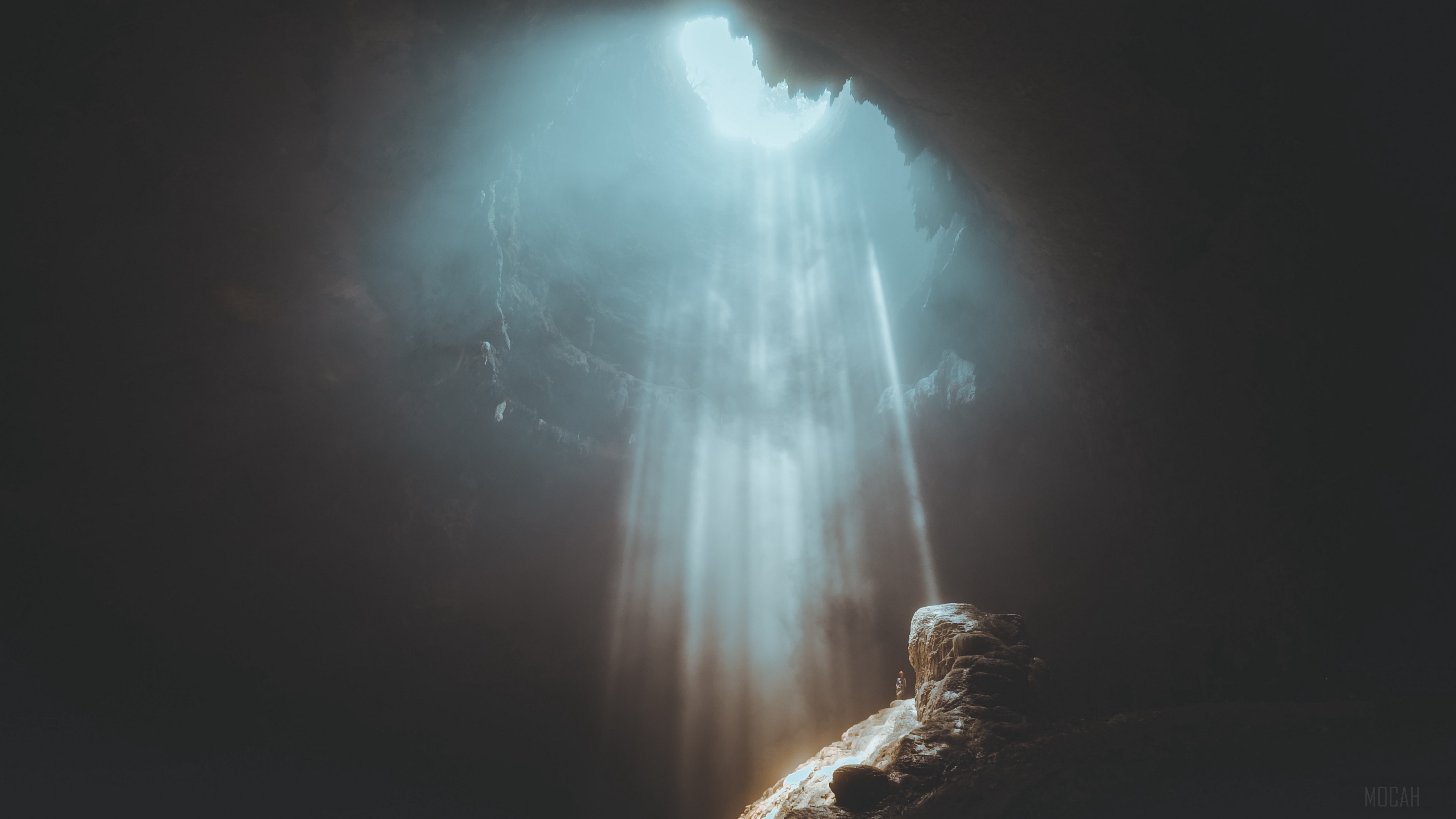 Sunlight beams into a dark cave with rocks HD Wallpaper