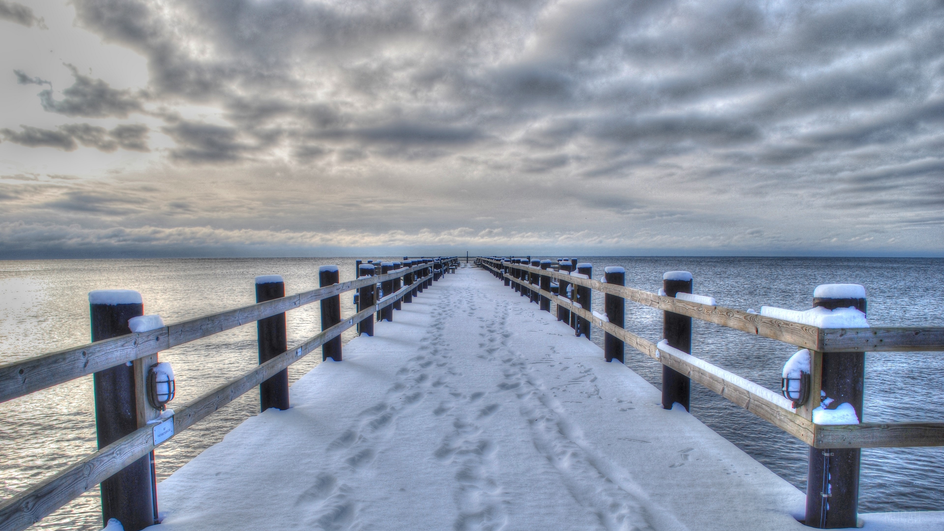 Snow-Covered Bridge Over Calm Sea in Winter 4K HD Wallpaper