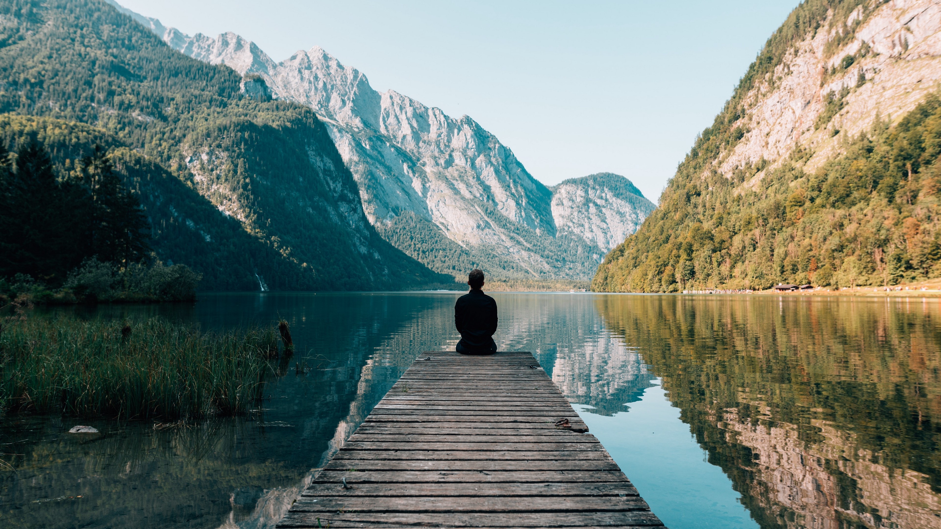 Man sitting on a pier overlooking mountains and lake HD Wallpaper