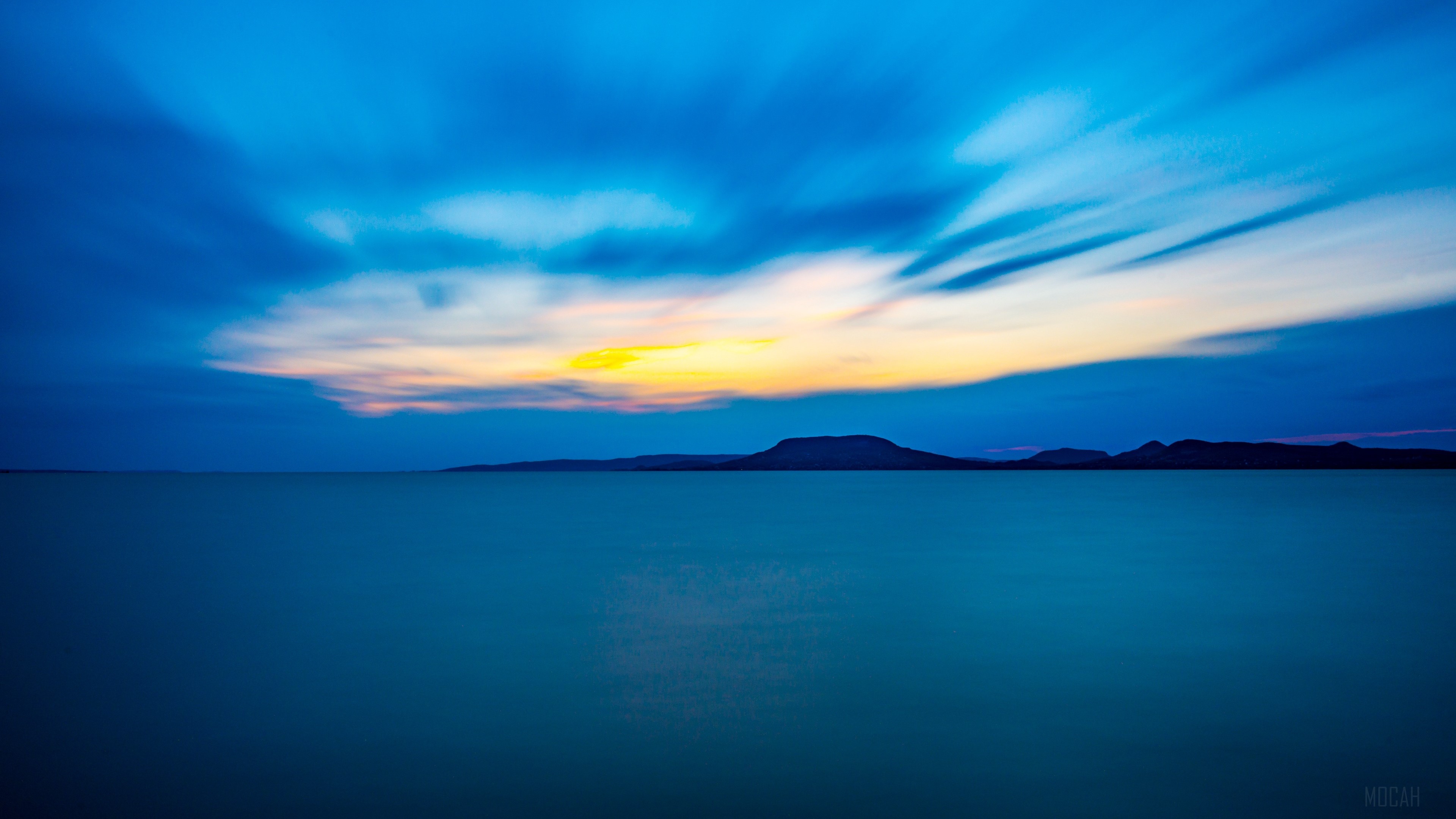 Blue sea and sky with distant mountains at sunset 4K HD Wallpaper