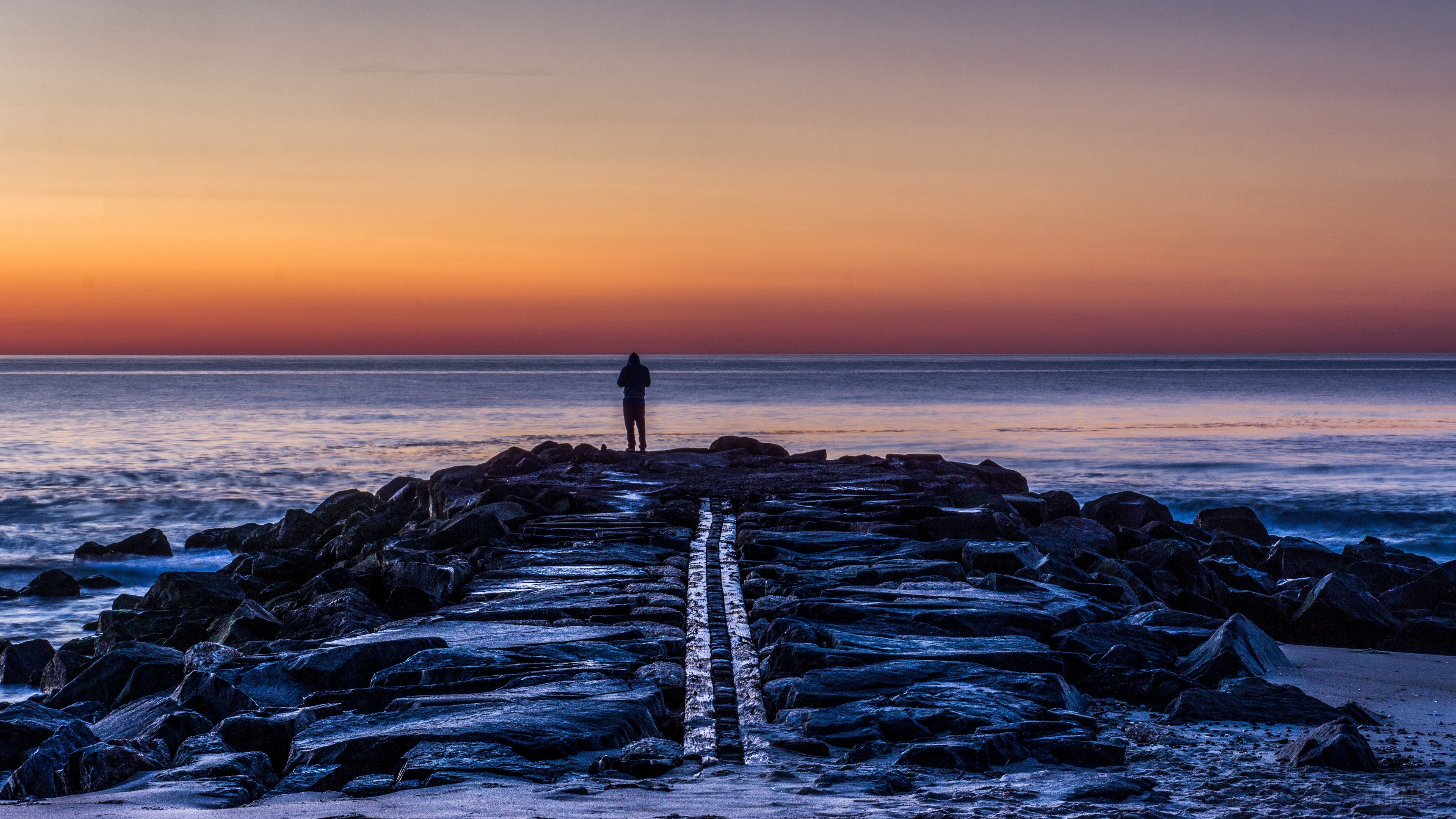 Man on a rocky shore at sunset 4K HD Wallpaper