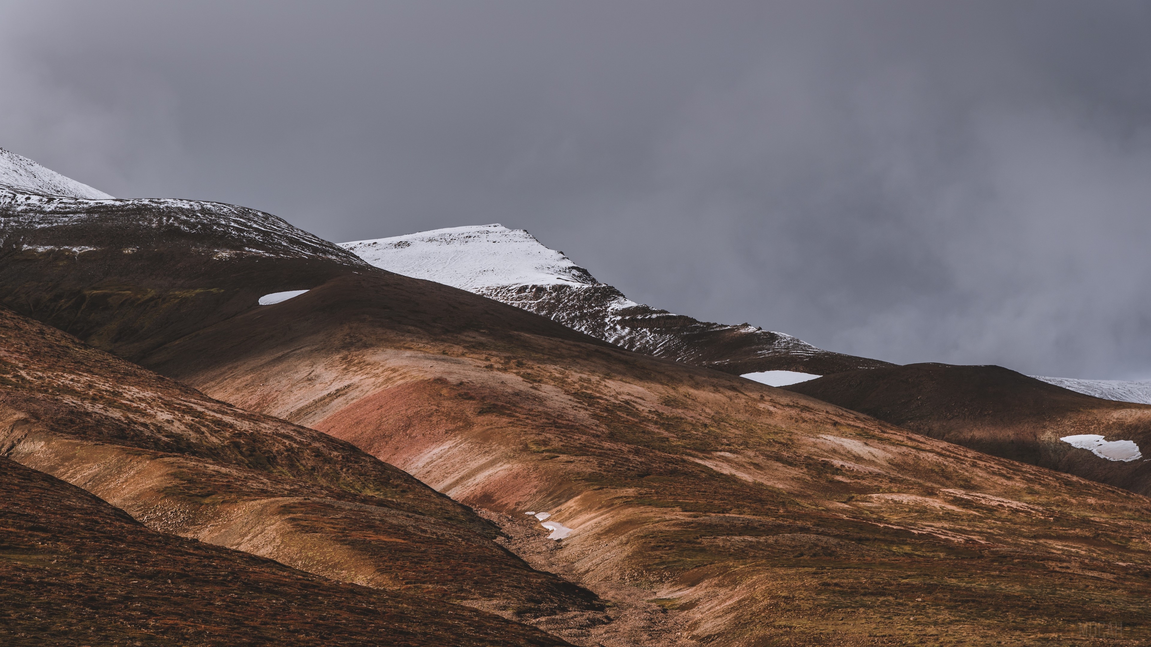 Snow-capped hills under a cloudy sky in Iceland HD Wallpaper
