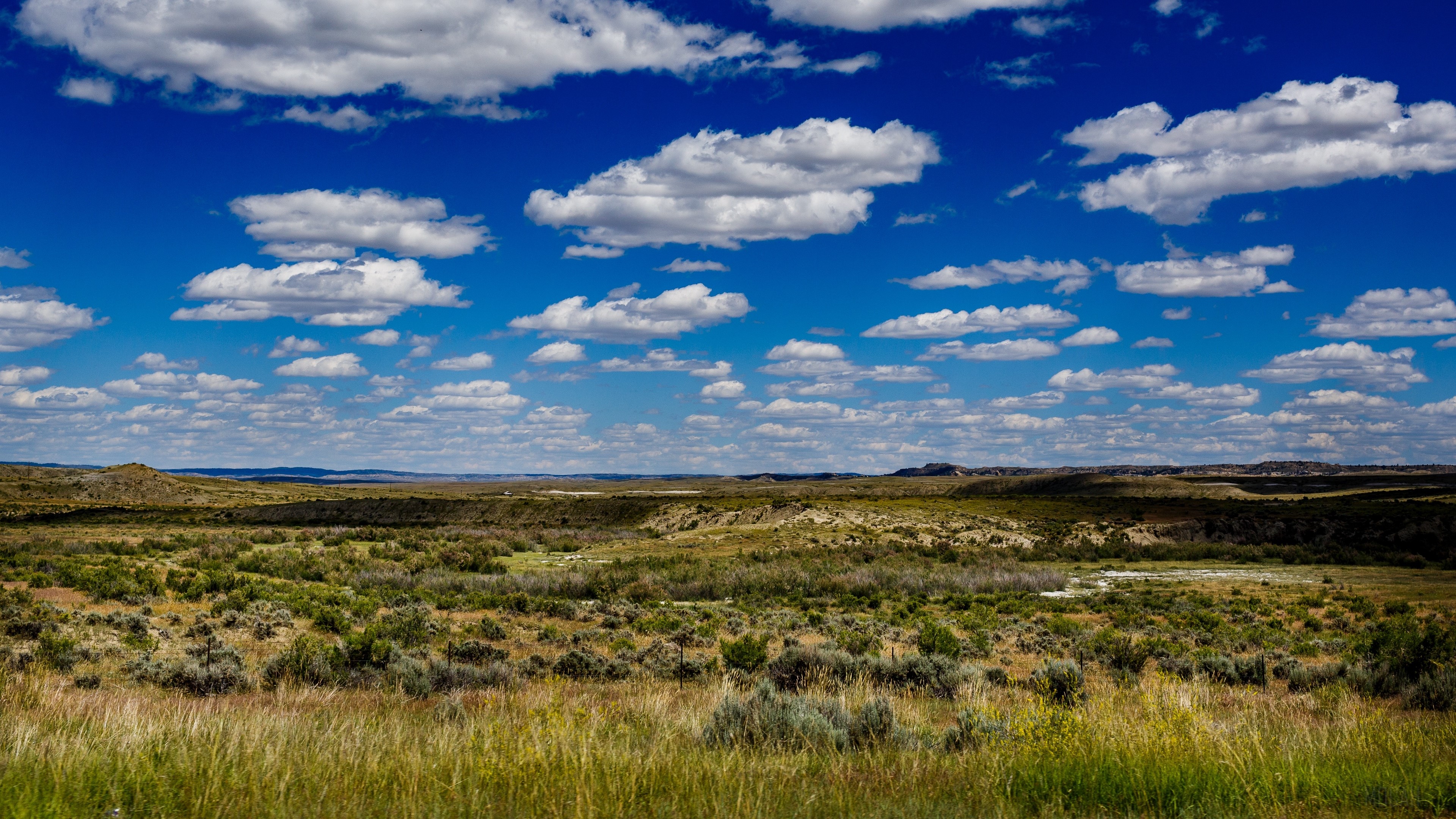 Vast landscape with rolling hills and scattered clouds HD Wallpaper