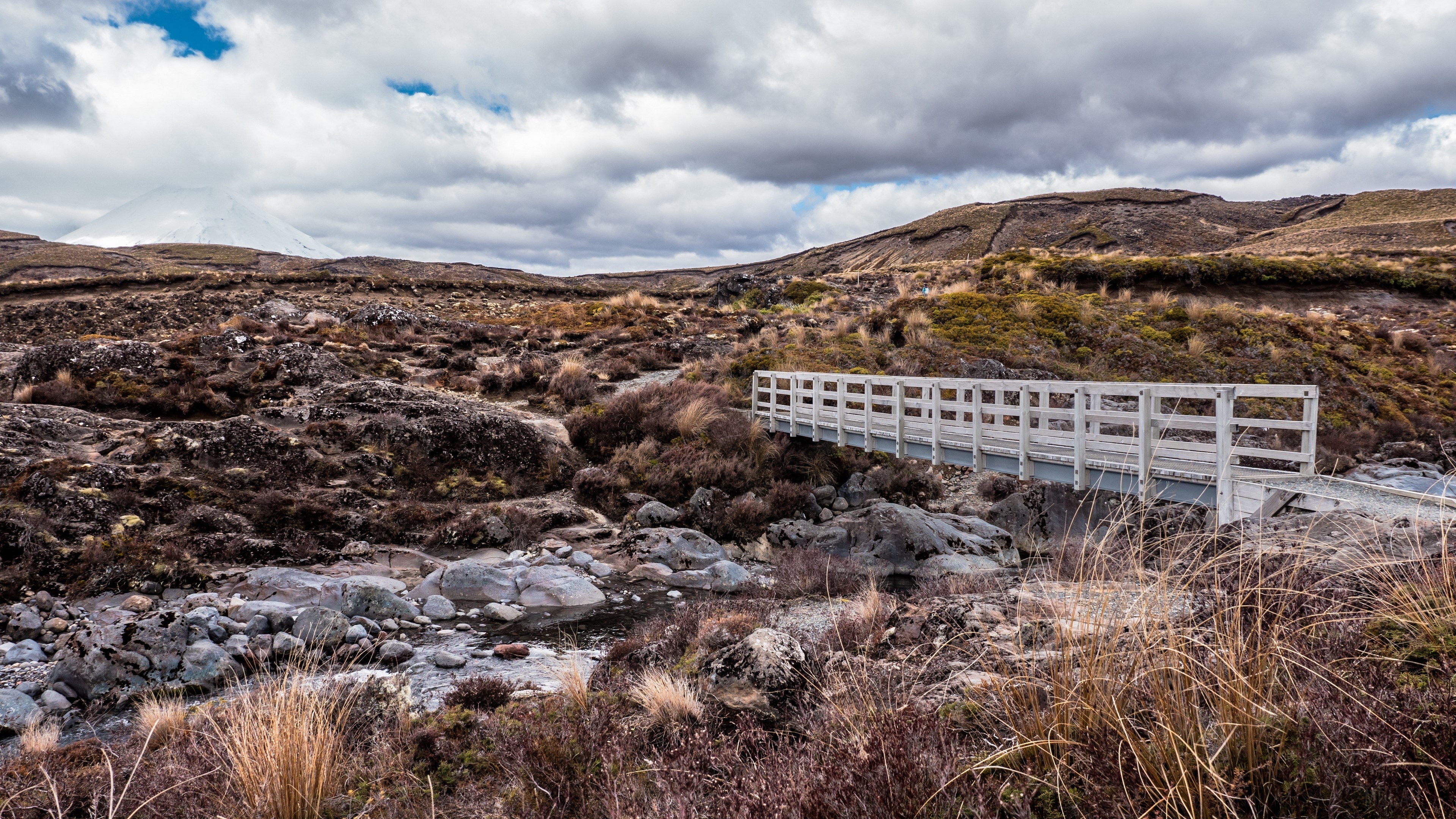 Bridge over rocky river with mountain in background 4K HD Wallpaper