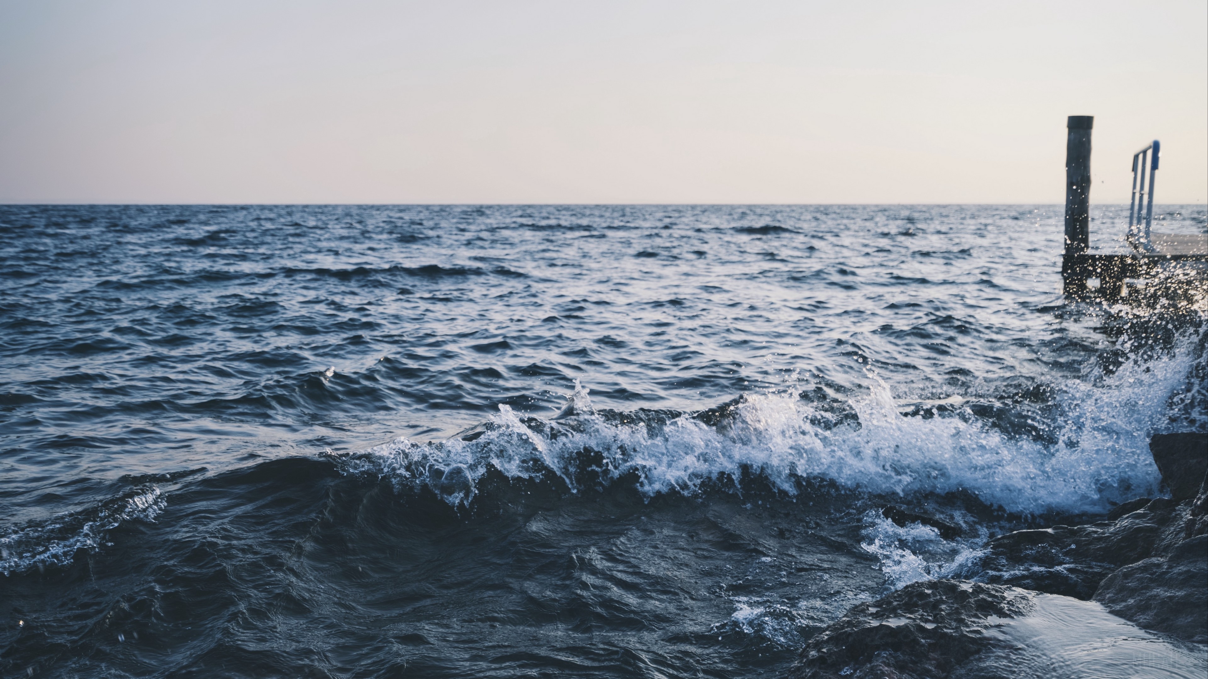 Sea with waves crashing on rocks and a pier HD Wallpaper