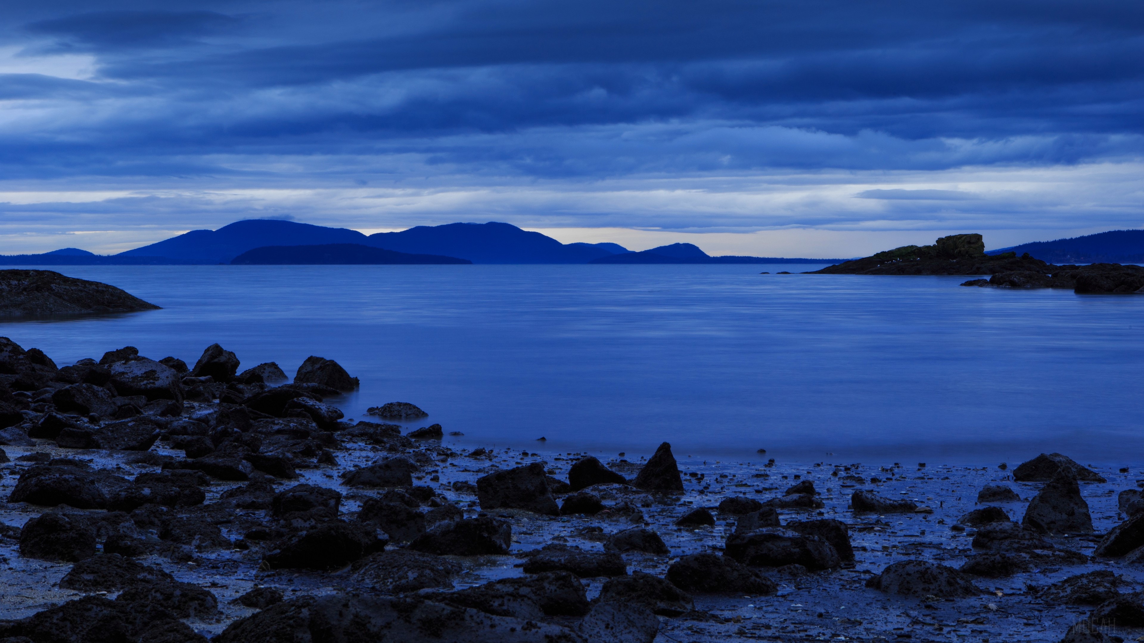 Rocky shore with mountains and ocean under cloudy sky 4K HD Wallpaper