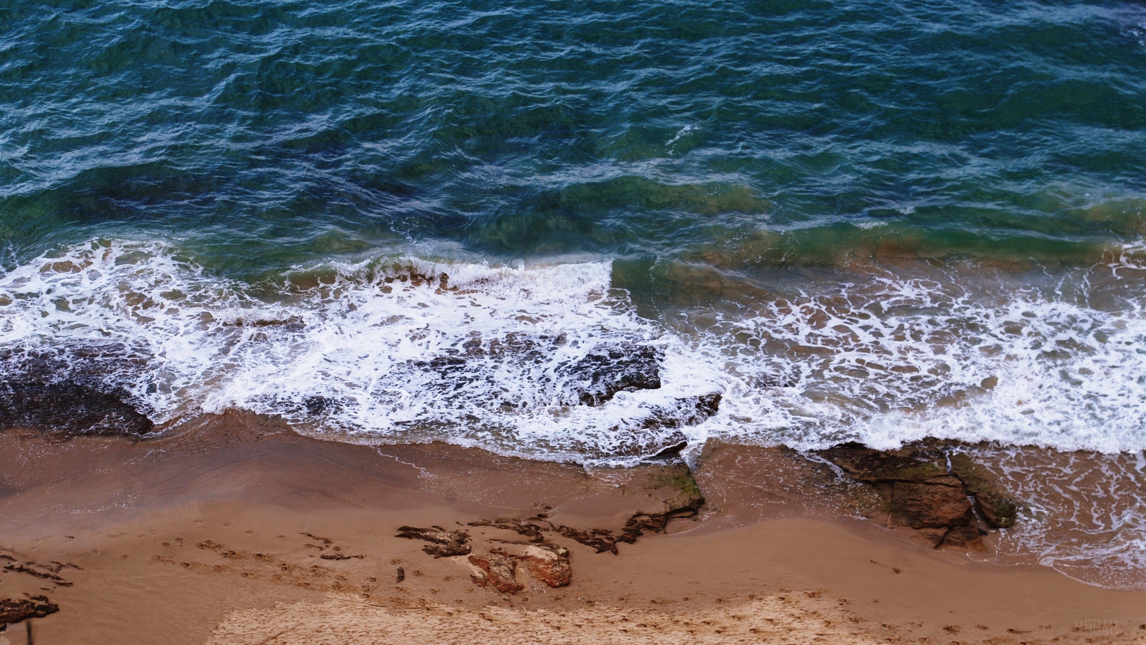 Ocean waves crashing on a sandy beach with footprints HD Wallpaper