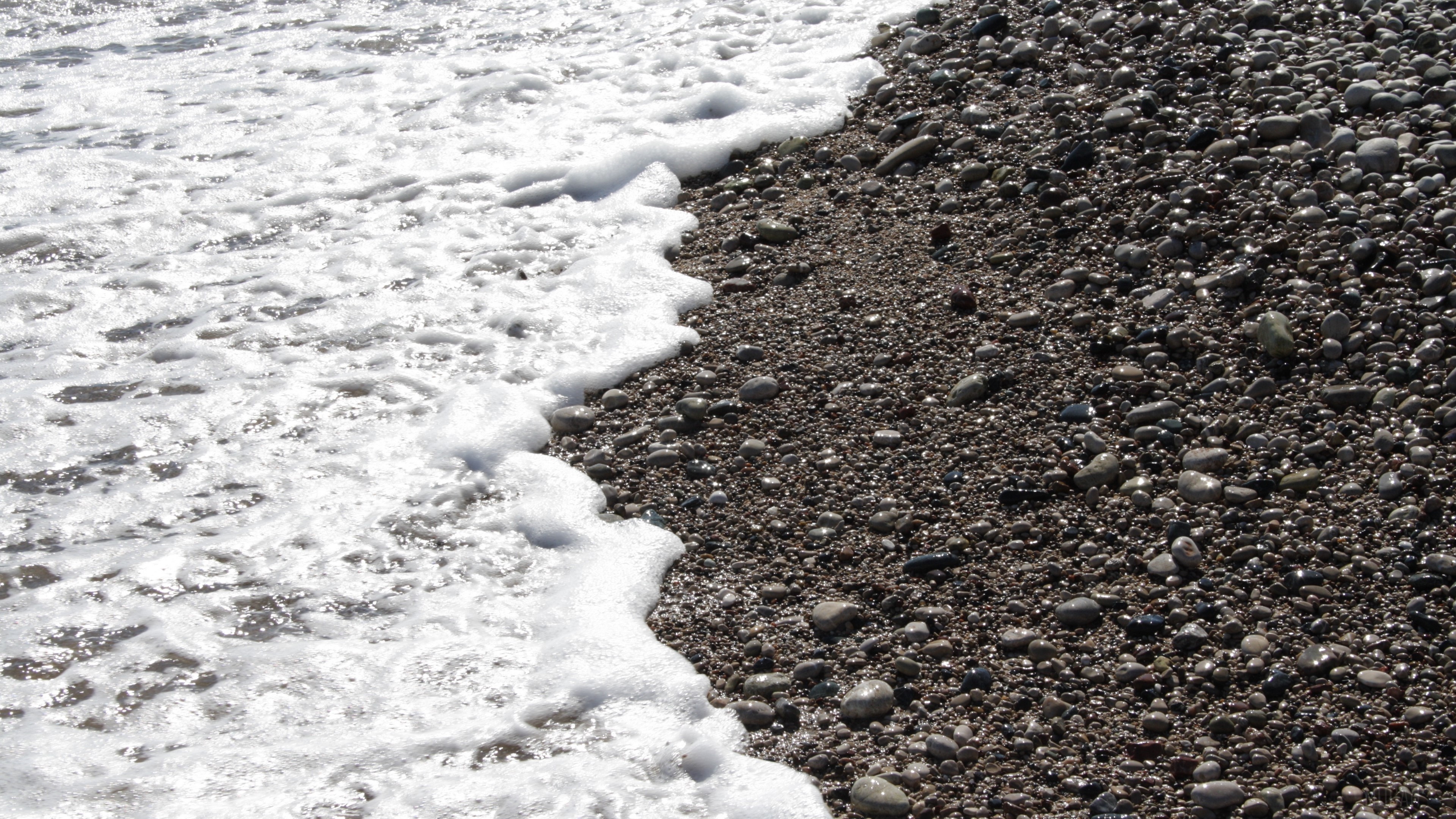 Sea foam washing over pebbles on a beach HD Wallpaper