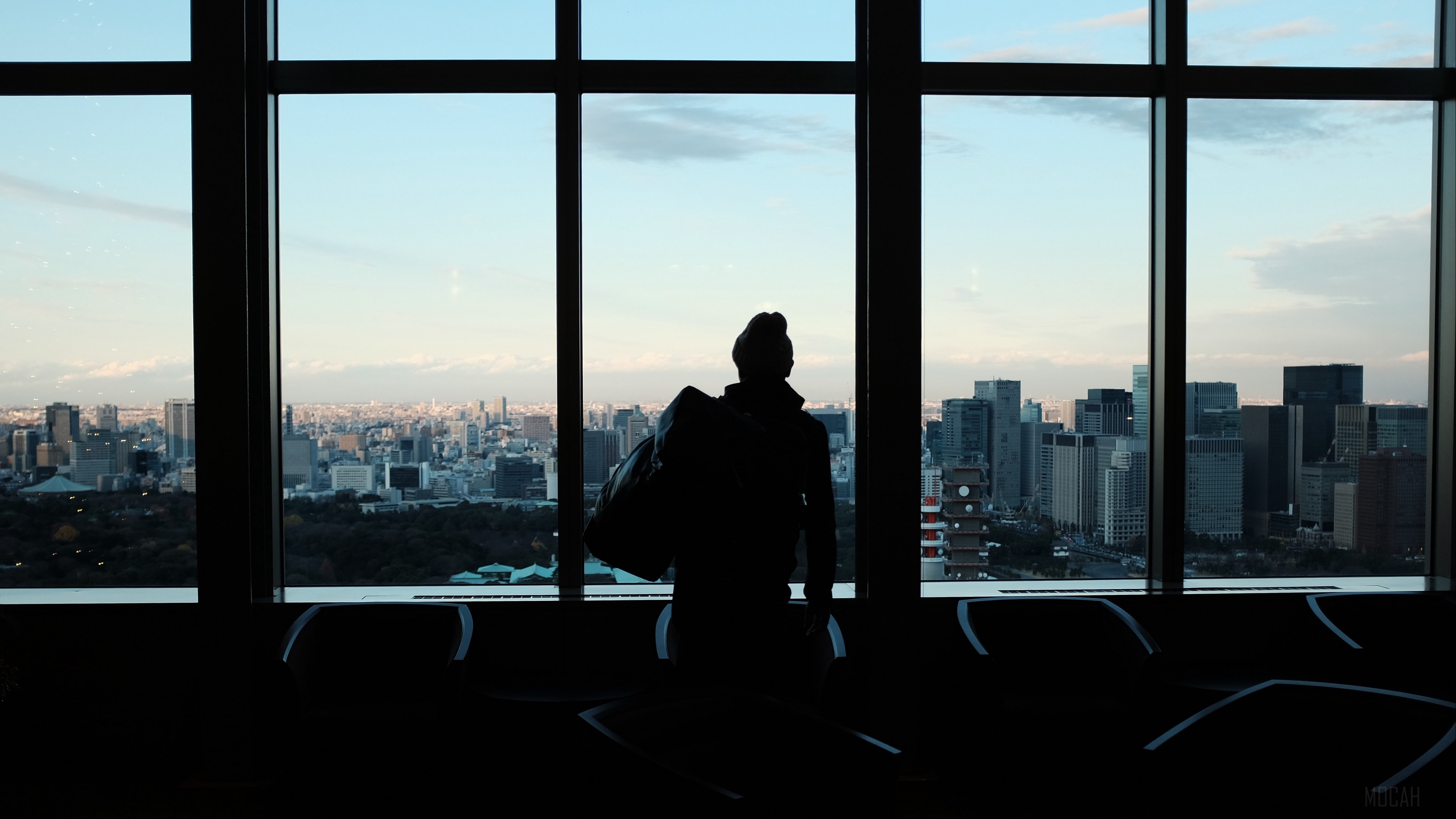 Silhouette of a person with a bag in front of a city view through a window 4K HD Wallpaper