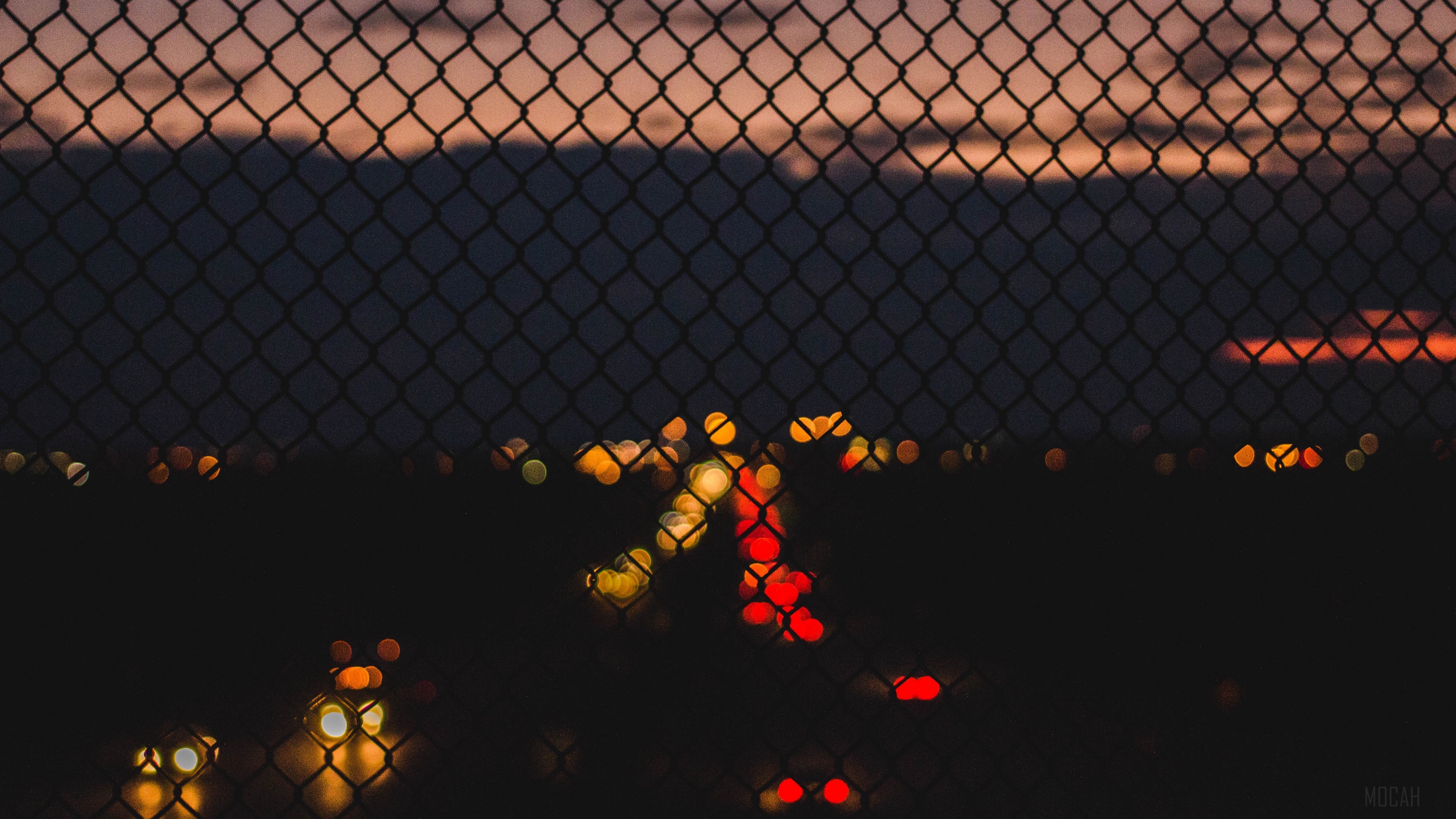 Bokeh lights through a chain-link fence at dusk HD Wallpaper