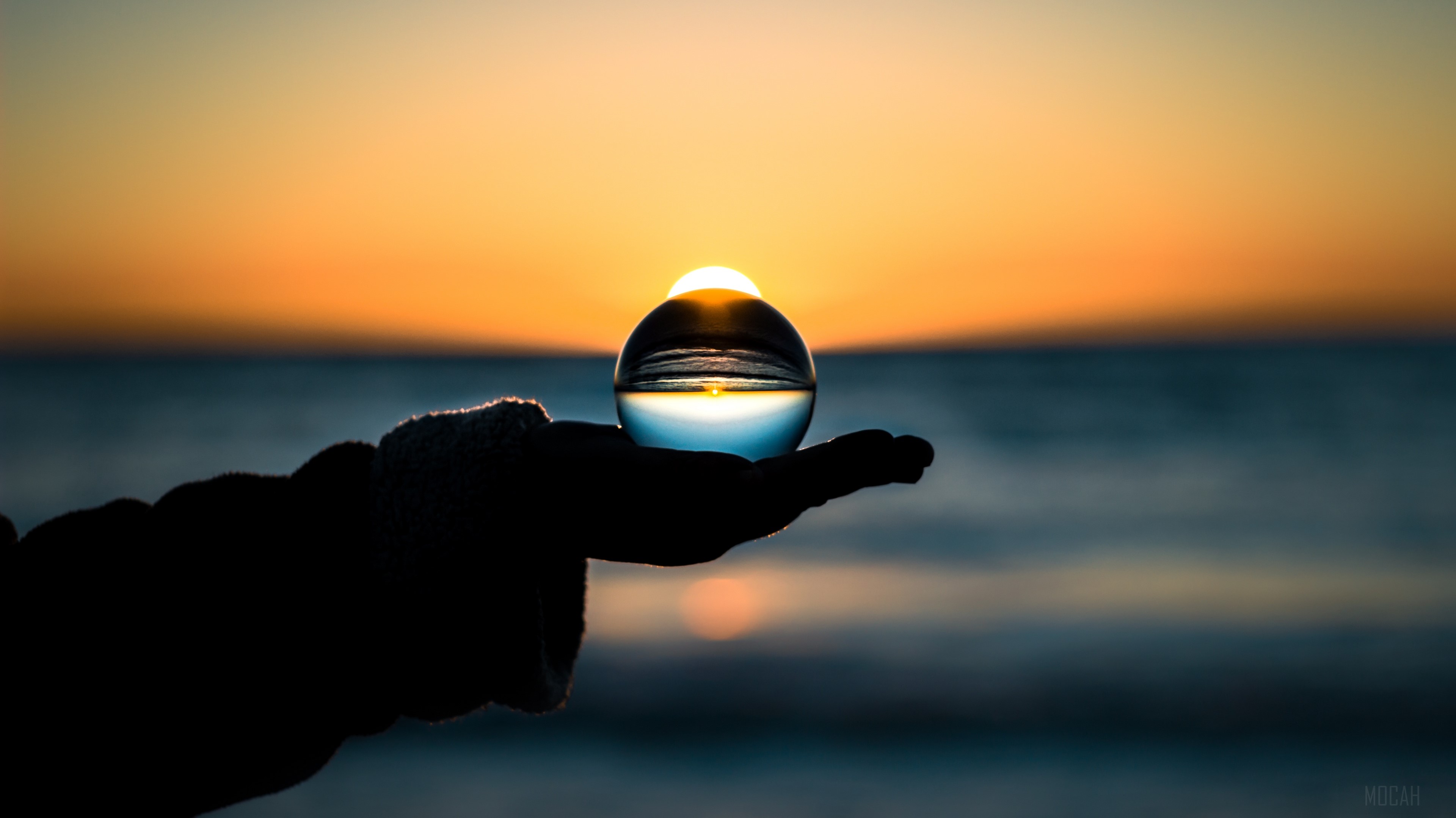 Sunset reflected in a glass ball held in a hand HD Wallpaper