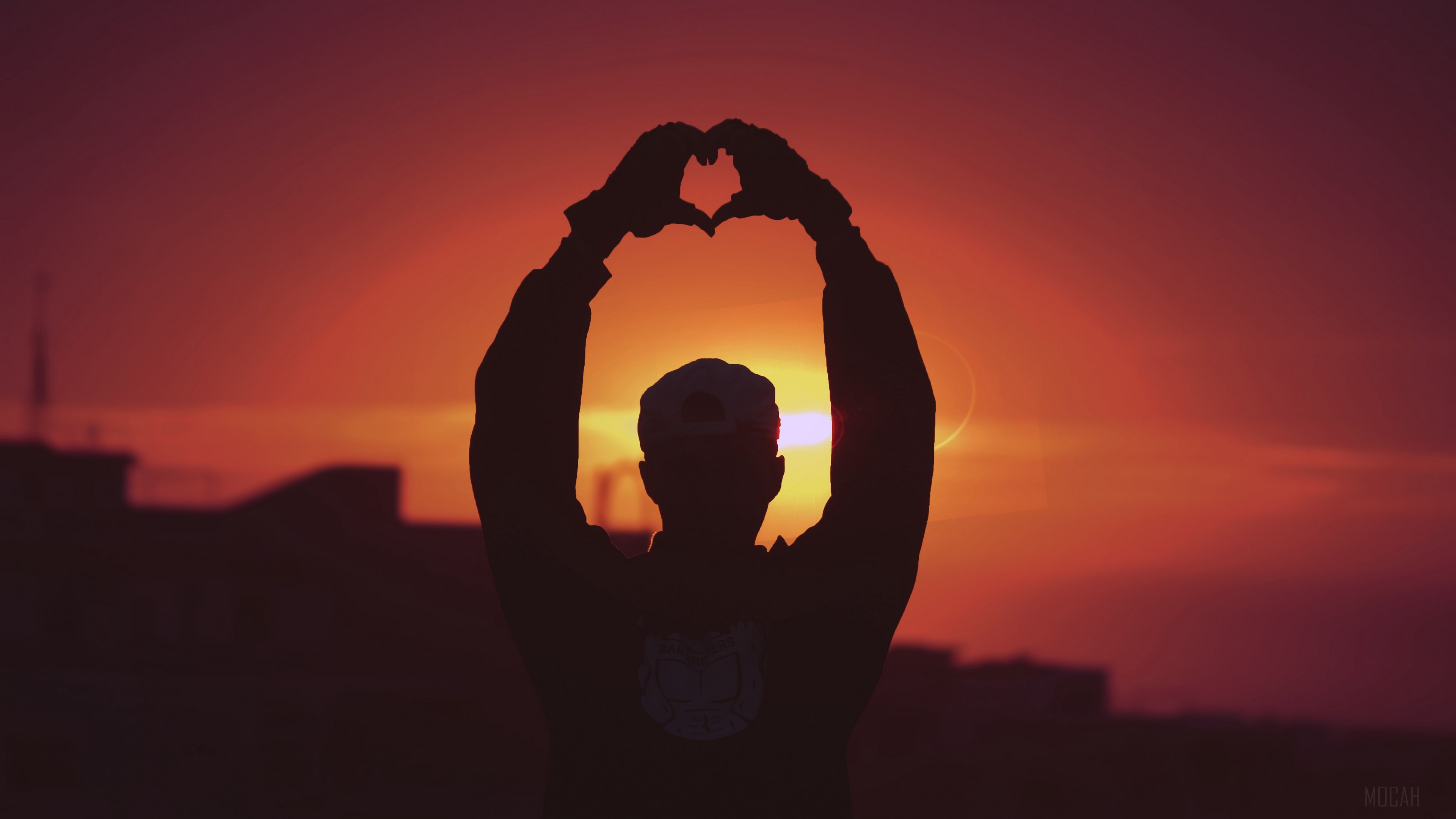 Man silhouetted against sunset making heart shape HD Wallpaper