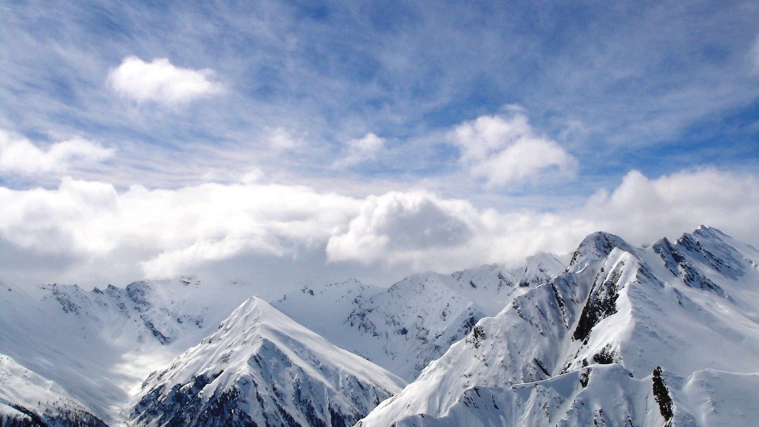 Snowy mountain peaks under a cloudy blue sky HD Wallpaper