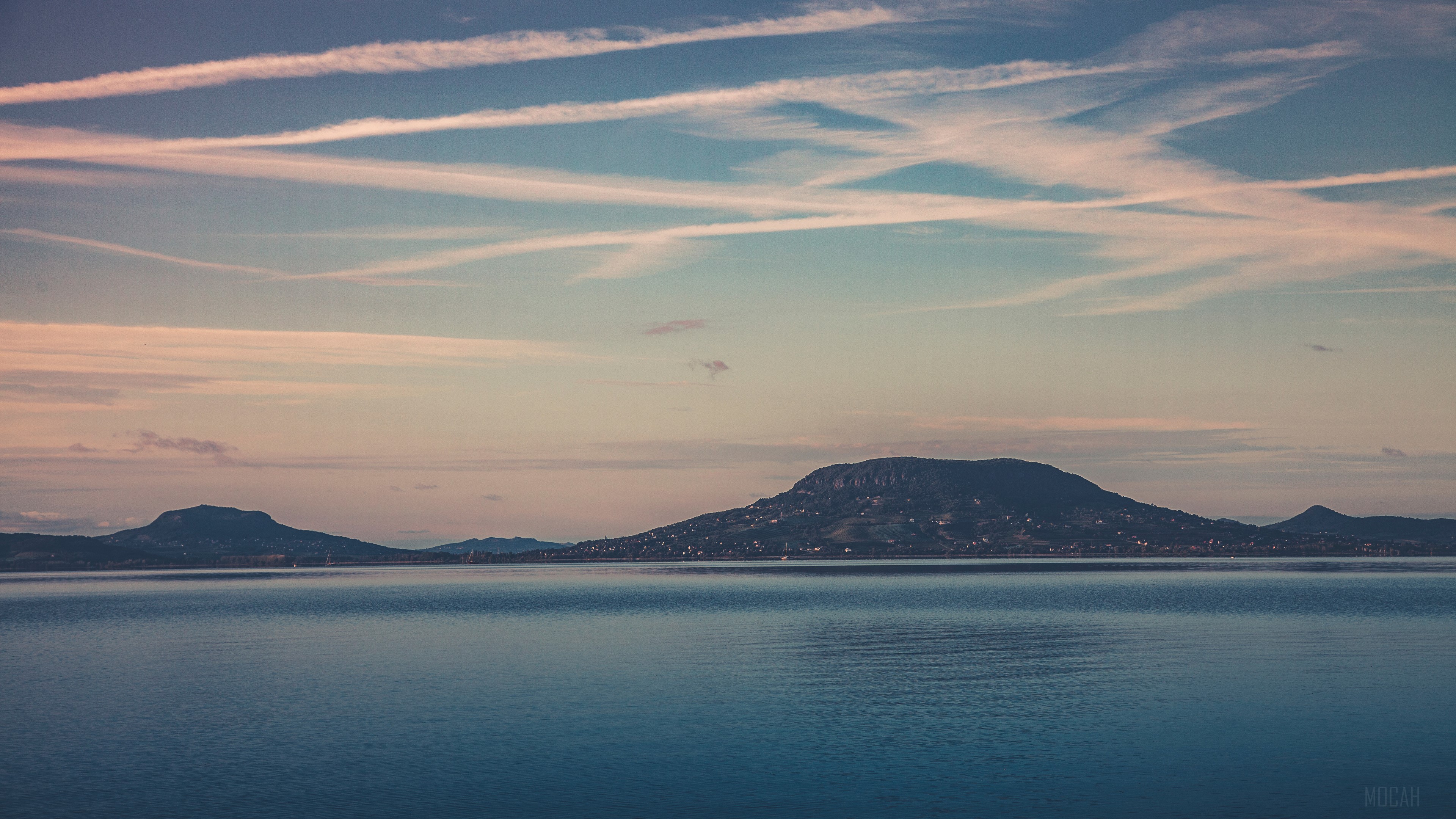 Mountains over a lake with contrails in the sky HD Wallpaper