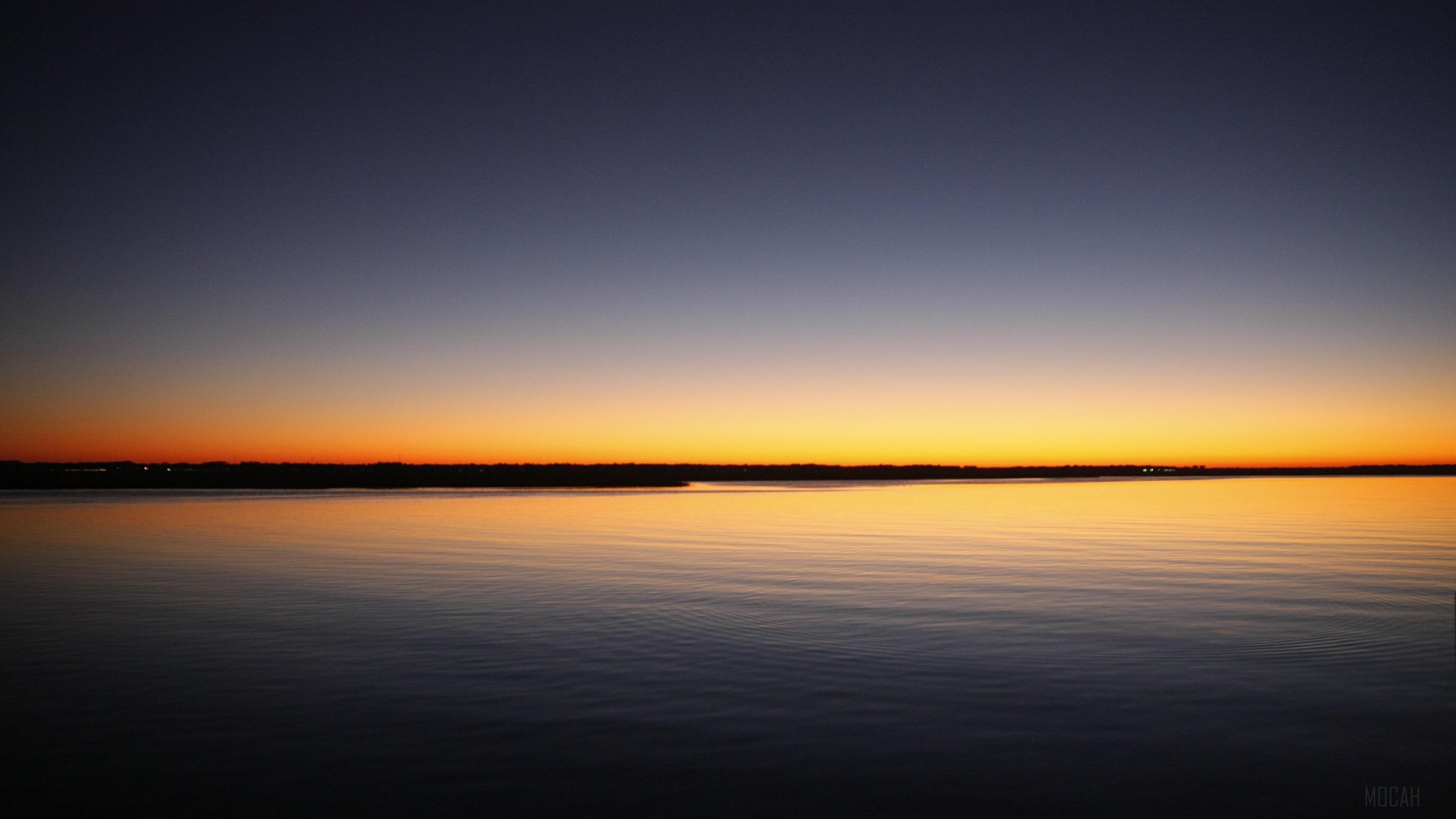 Sunset over a calm sea with a distant shoreline HD Wallpaper