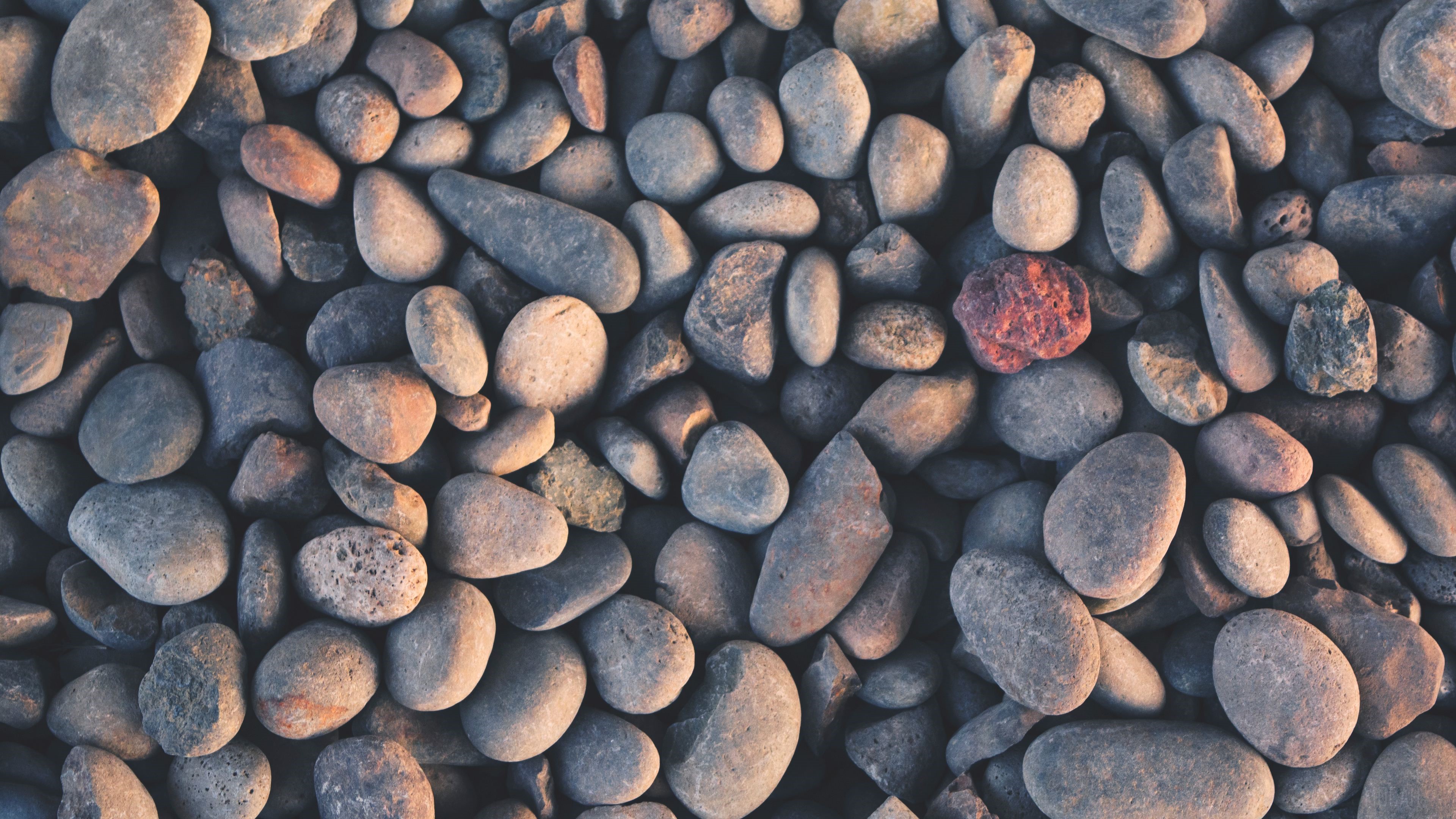 Close-up of assorted smooth river stones, one reddish stone prominent, 4K HD Wallpaper