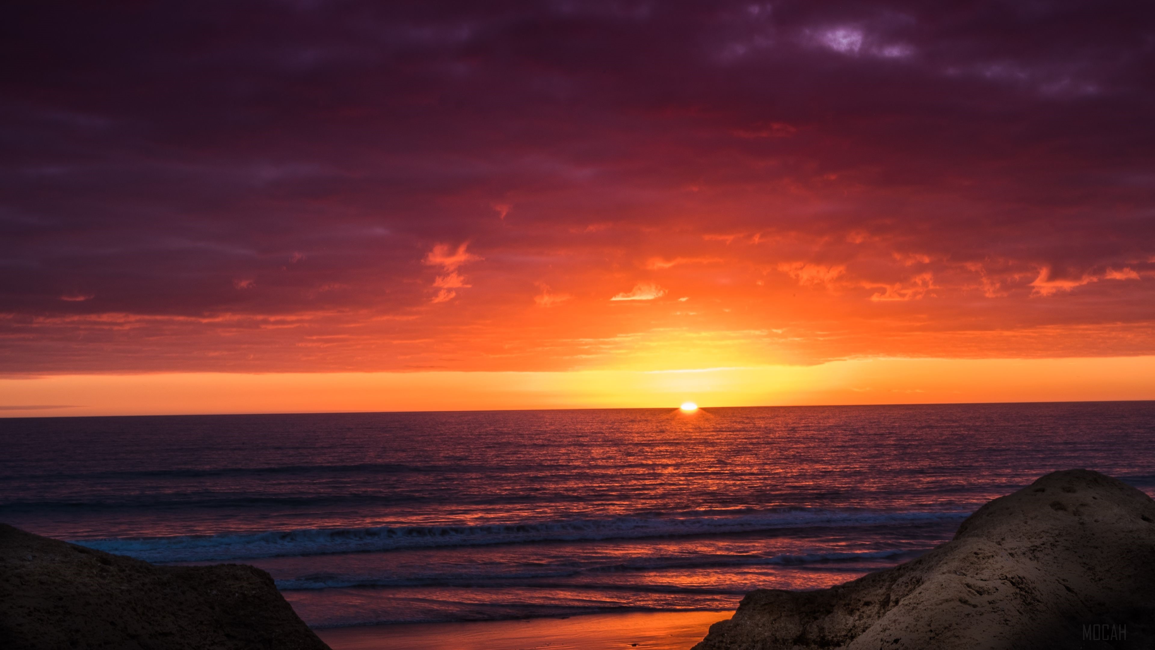 Sunset over the ocean with purple clouds and rocks HD Wallpaper