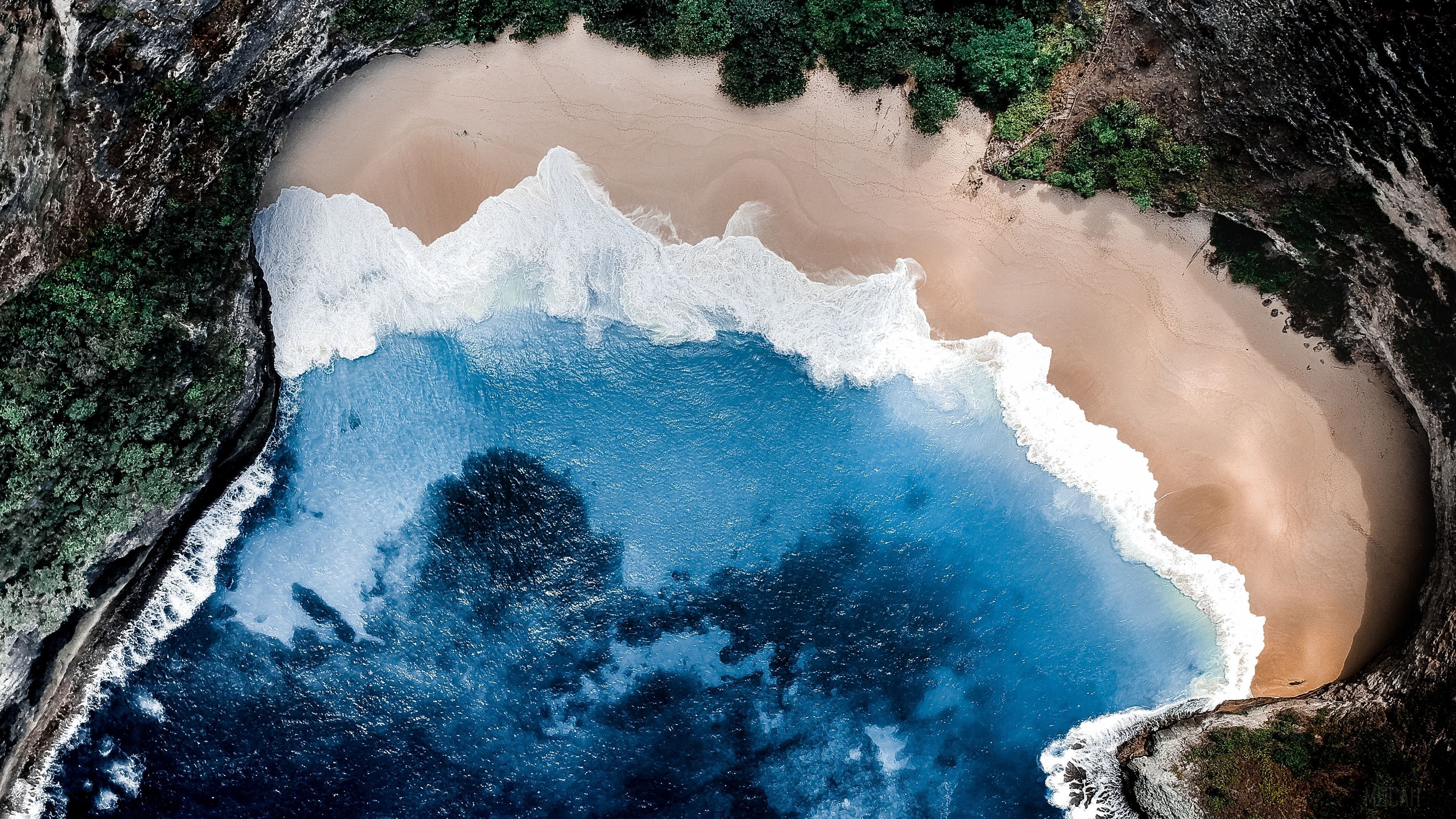 Aerial view of a secluded beach cove with turquoise water and lush green cliffs HD Wallpaper
