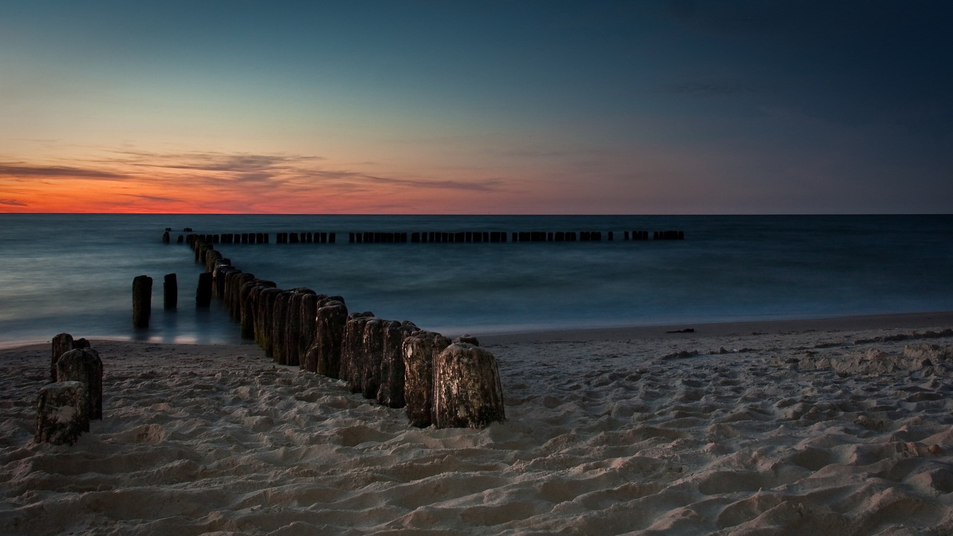 Wooden breakwaters on a sandy beach at sunset HD Wallpaper