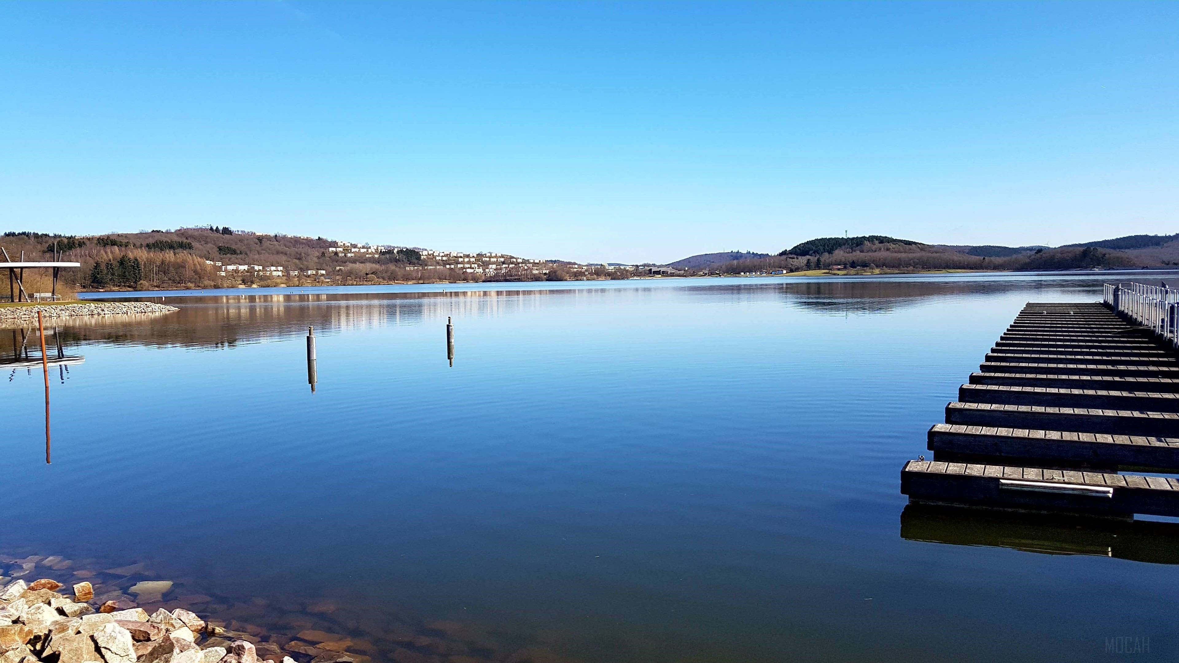 Lake with a wooden dock and distant houses HD Wallpaper