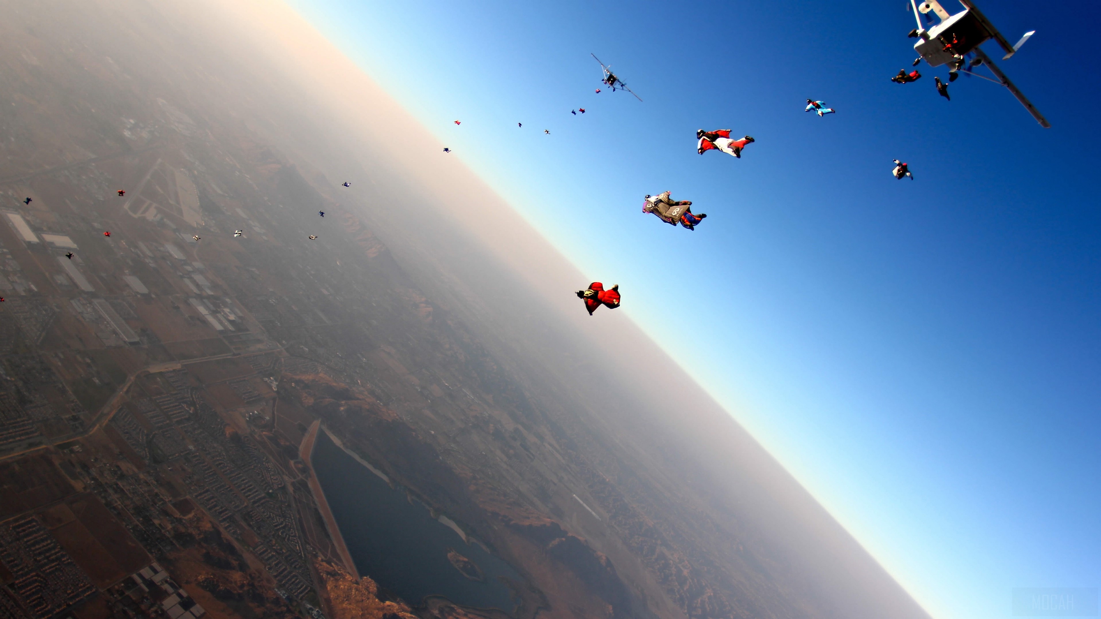 Wingsuit jumpers flying near a plane over a city HD Wallpaper