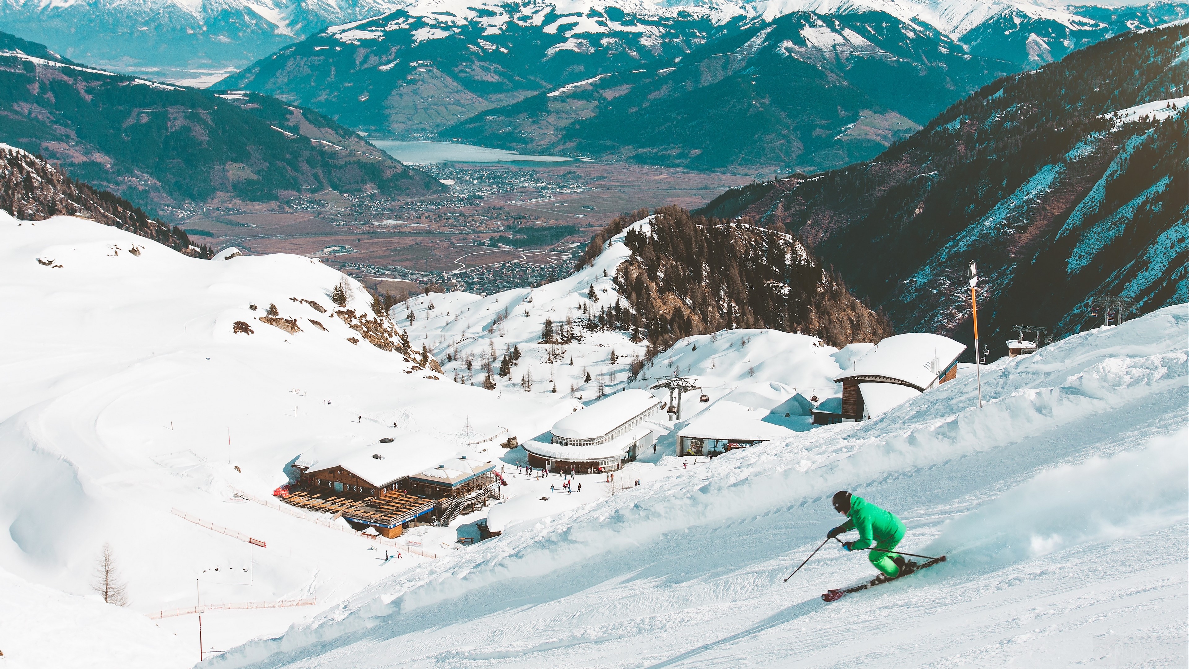 Skier on a snowy mountain with a village in the valley HD Wallpaper