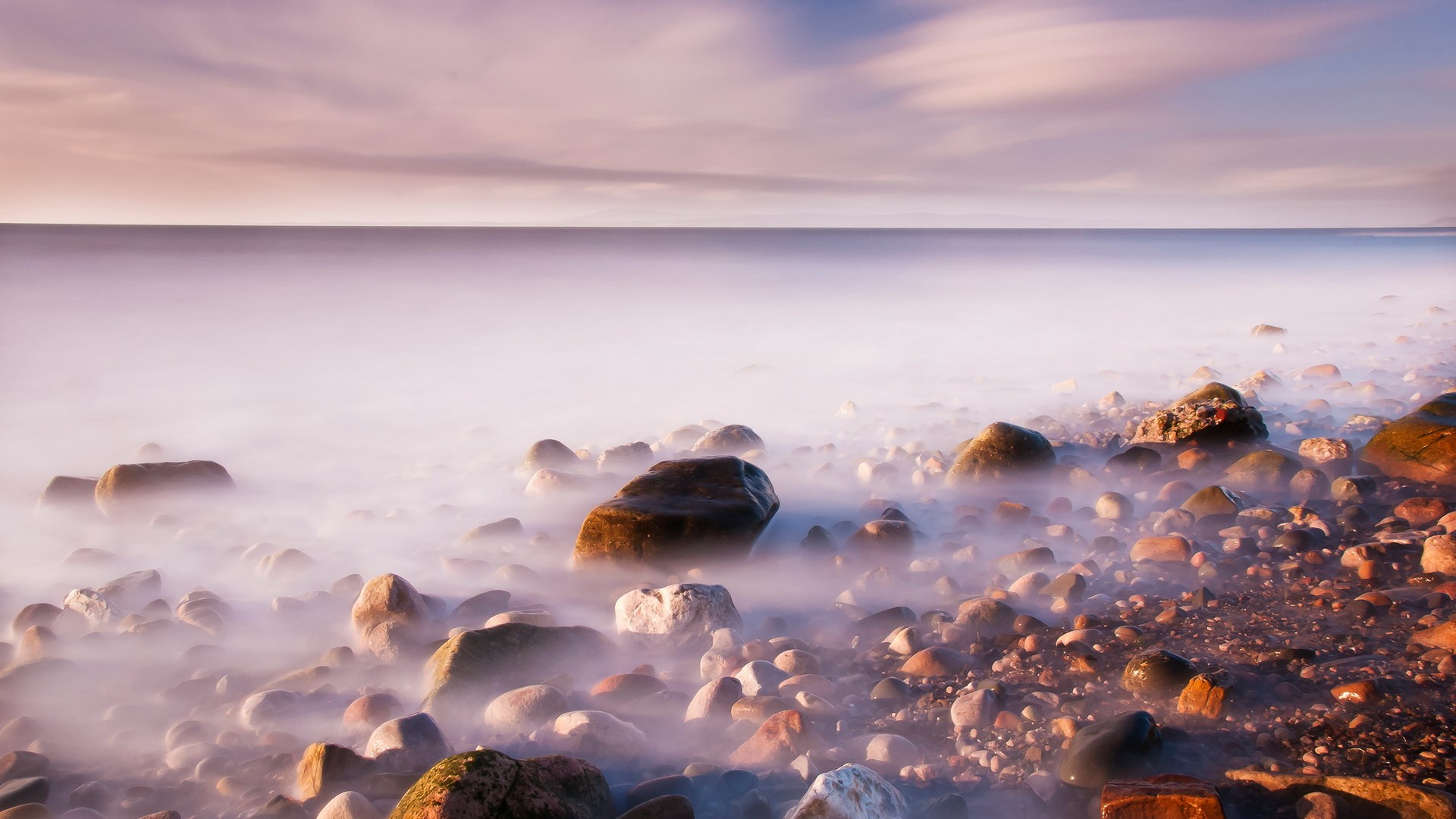 Long exposure of a rocky shore with misty water HD Wallpaper