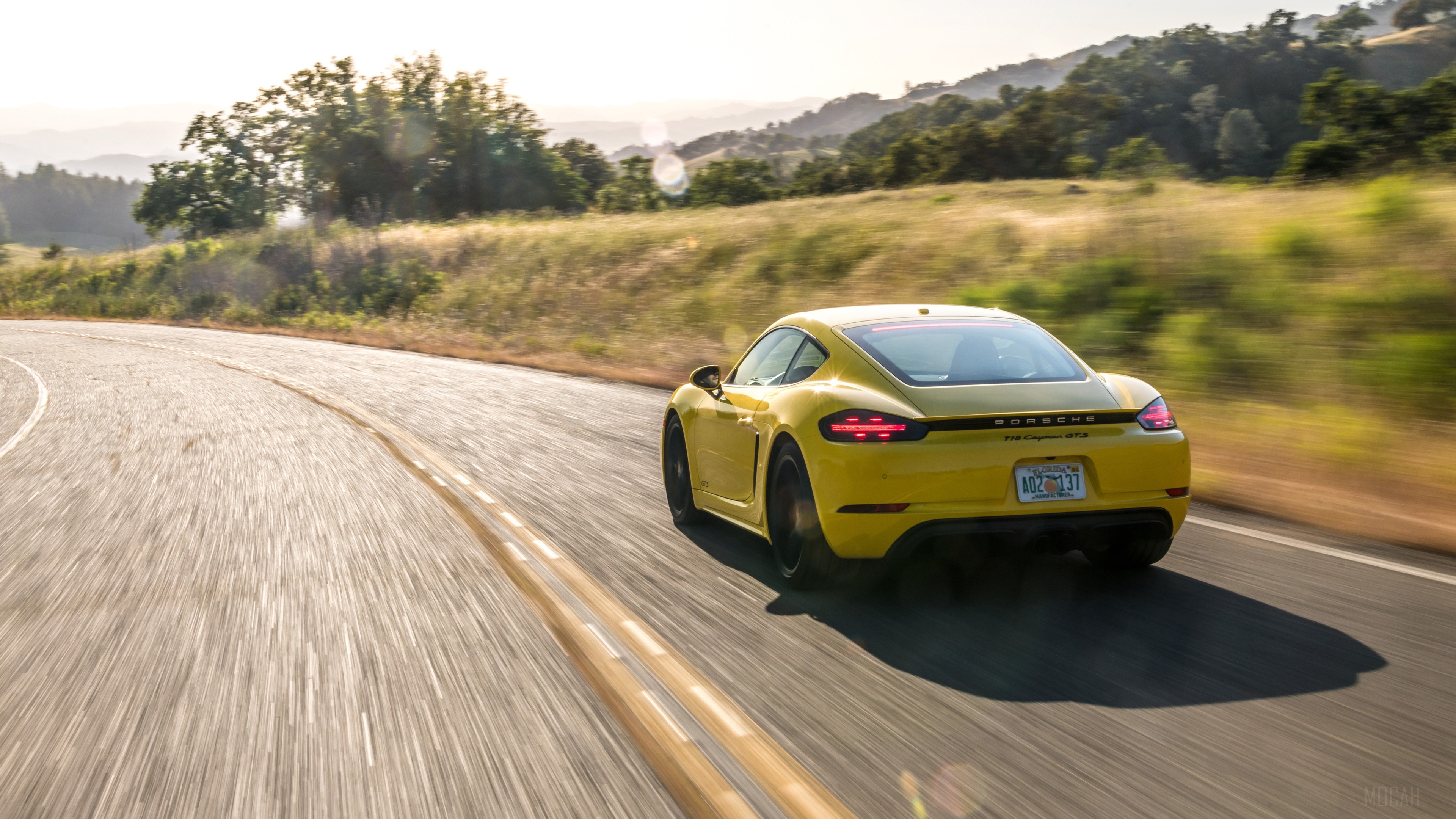 Yellow Porsche 718 Cayman GTS driving on a winding road HD Wallpaper
