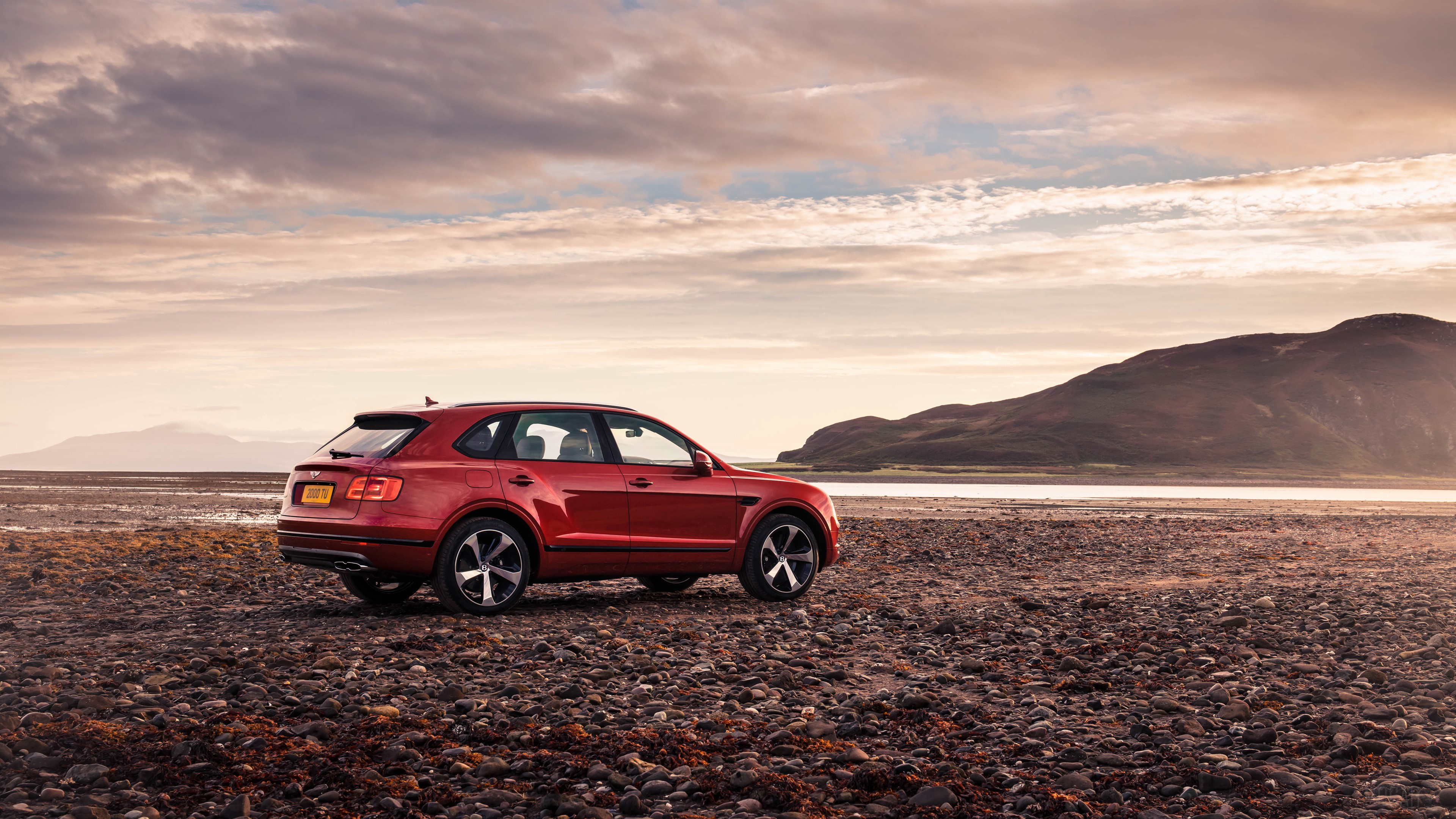 Red Bentley Bentayga V8 2018 parked on rocky shore HD Wallpaper