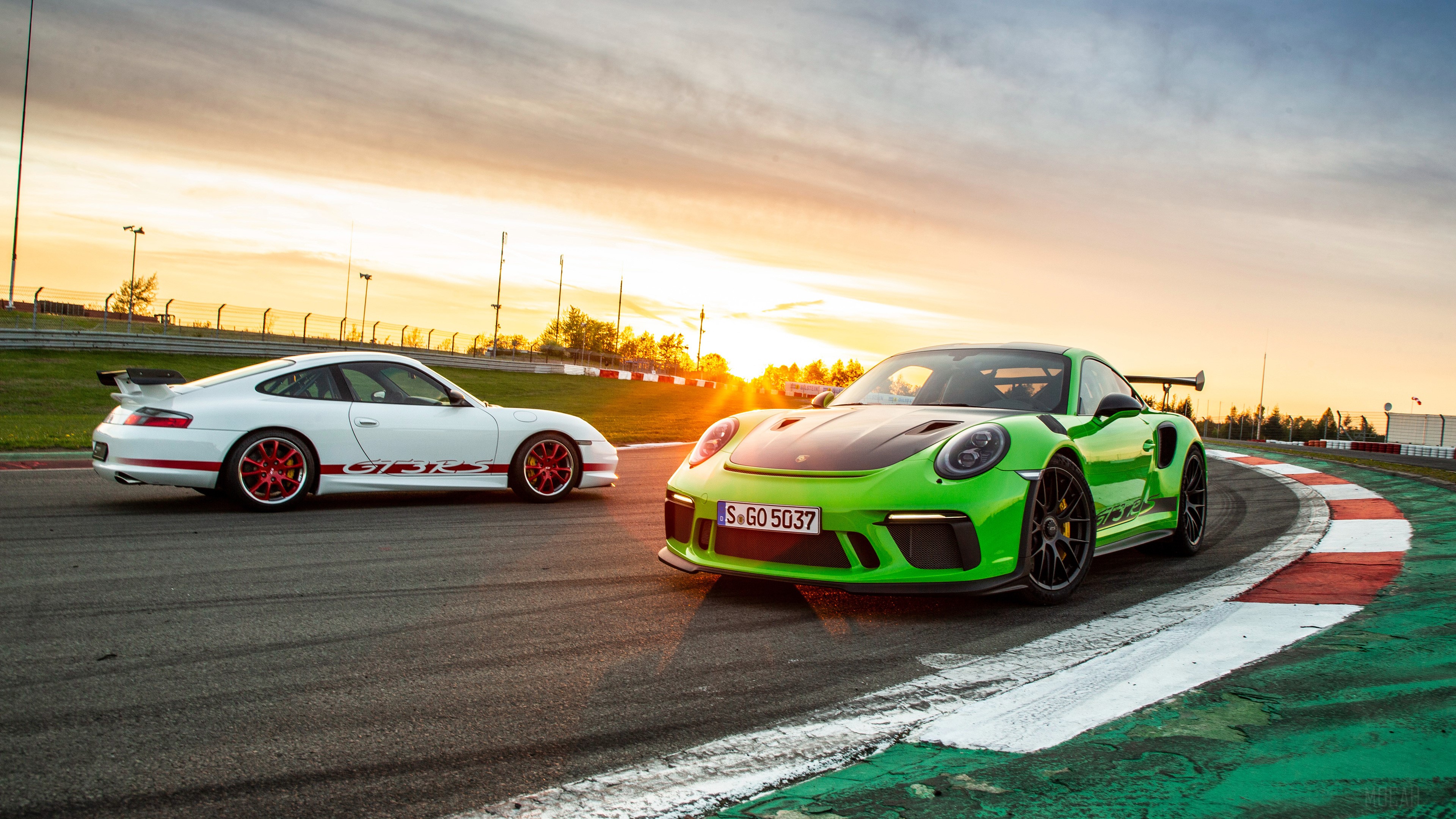 Two Porsche 911 cars on a race track at sunset HD Wallpaper