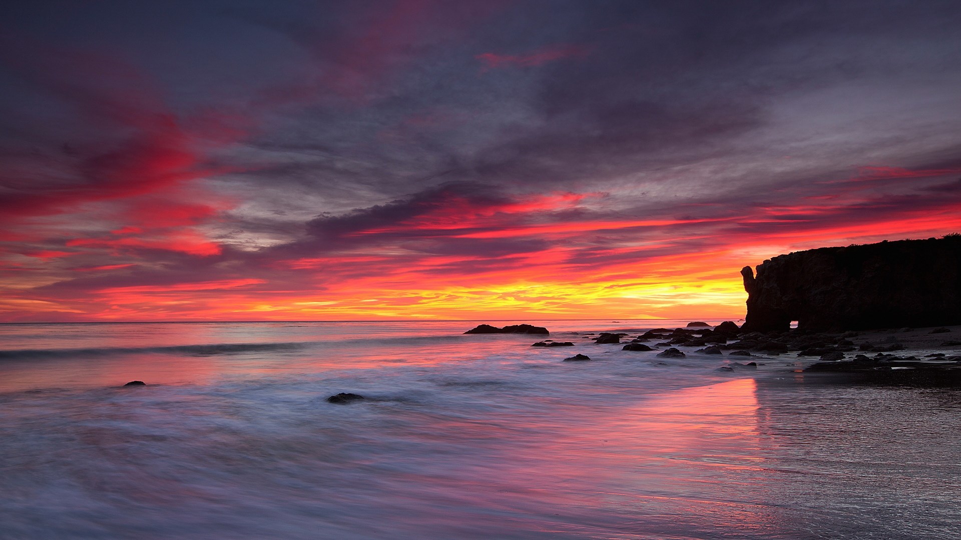 Sunset over the ocean with dramatic clouds and rocky shore HD Wallpaper