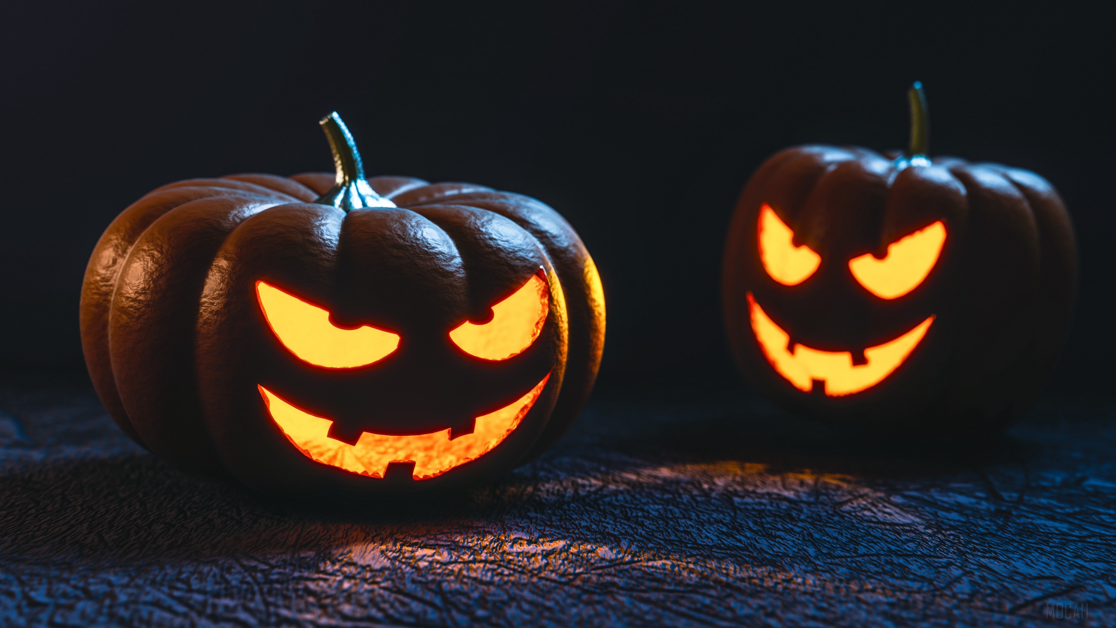 Two carved pumpkins with glowing faces on a dark surface HD Wallpaper