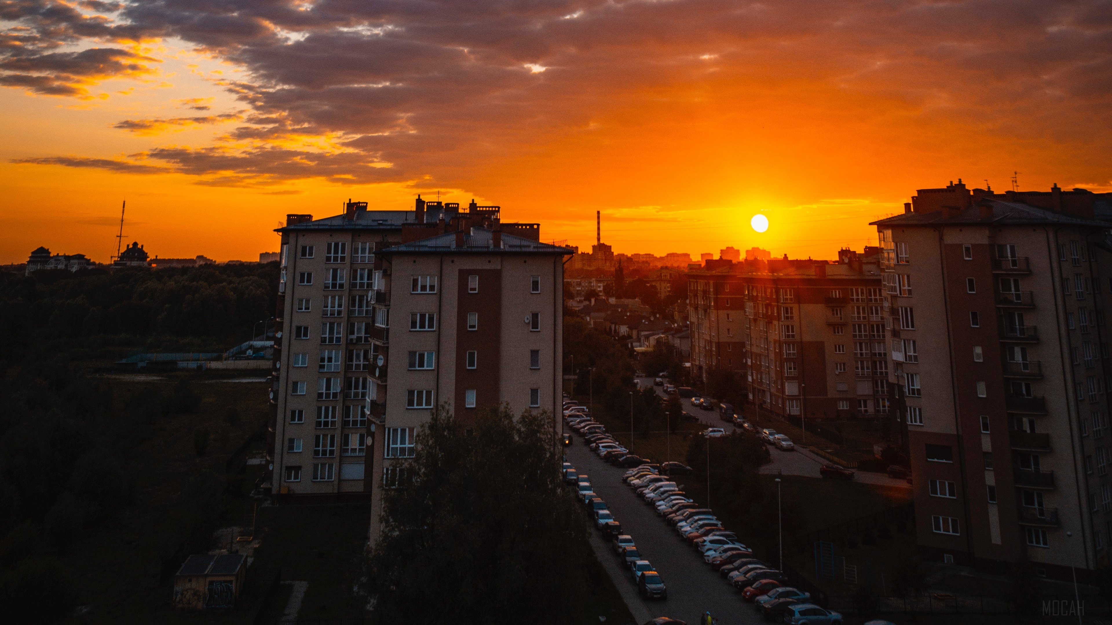 City buildings at sunset with clouds and parking HD Wallpaper