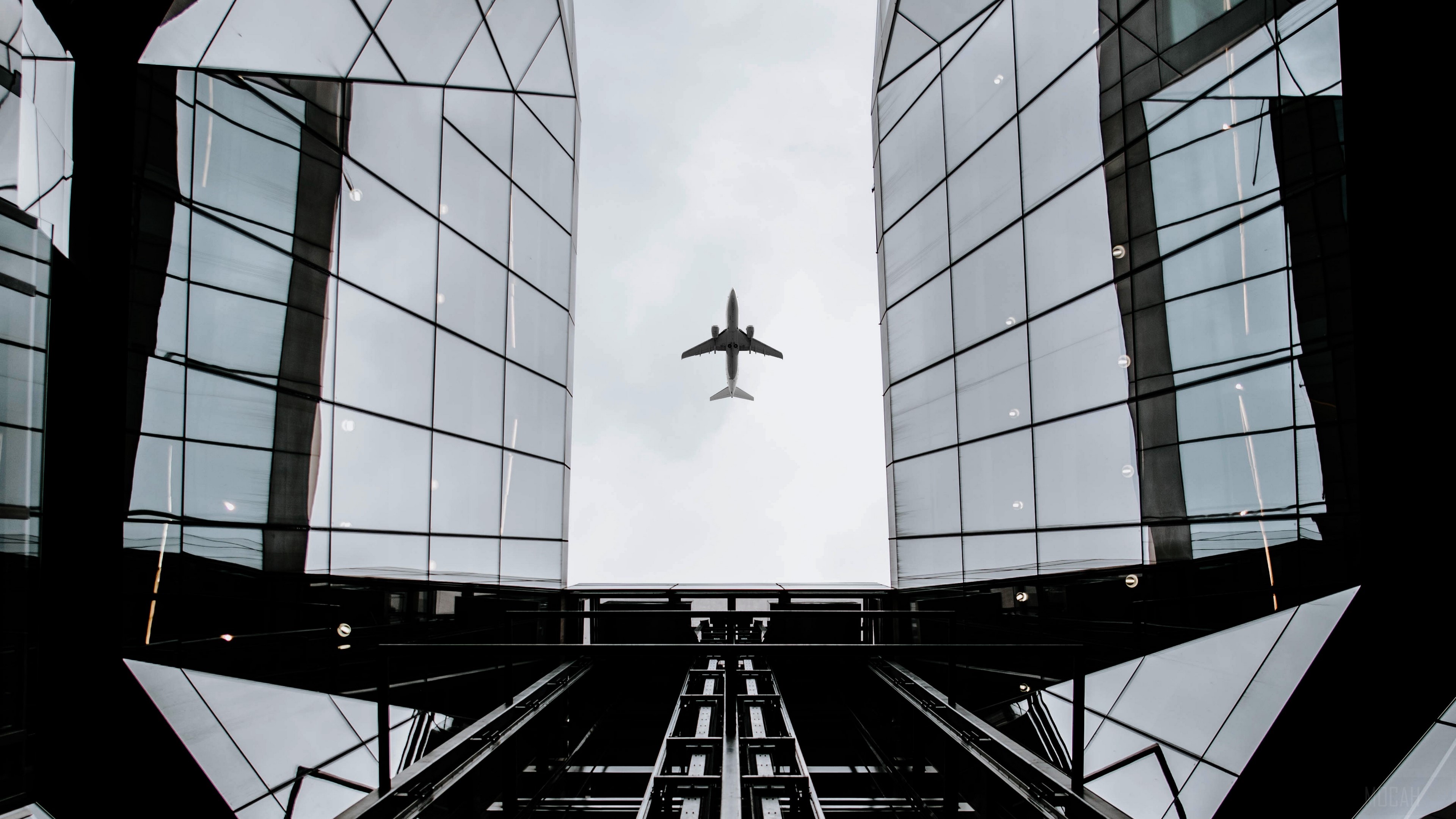Airplane flying between modern buildings, bottom view HD Wallpaper
