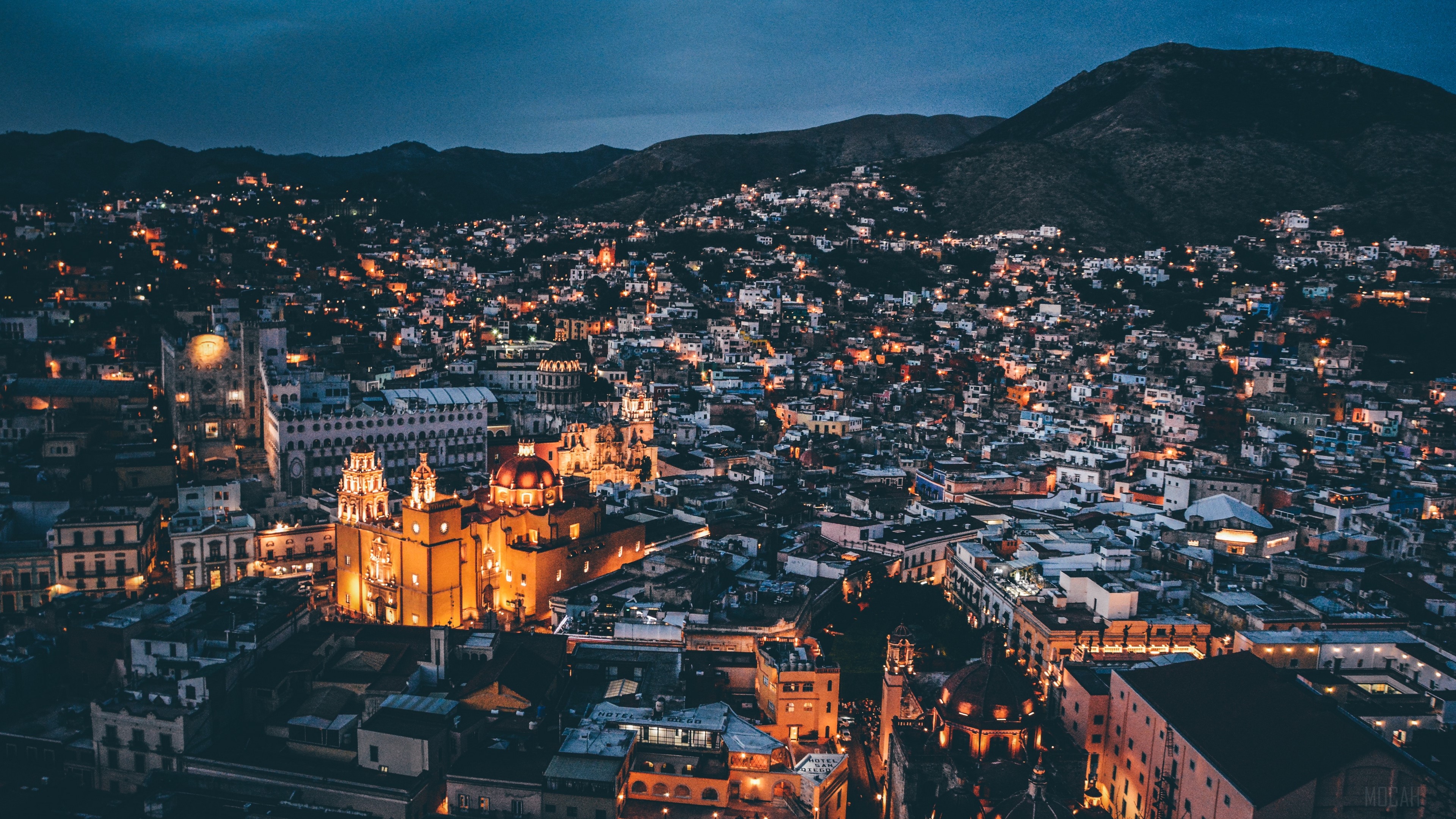 Night city view with illuminated buildings and mountains HD Wallpaper