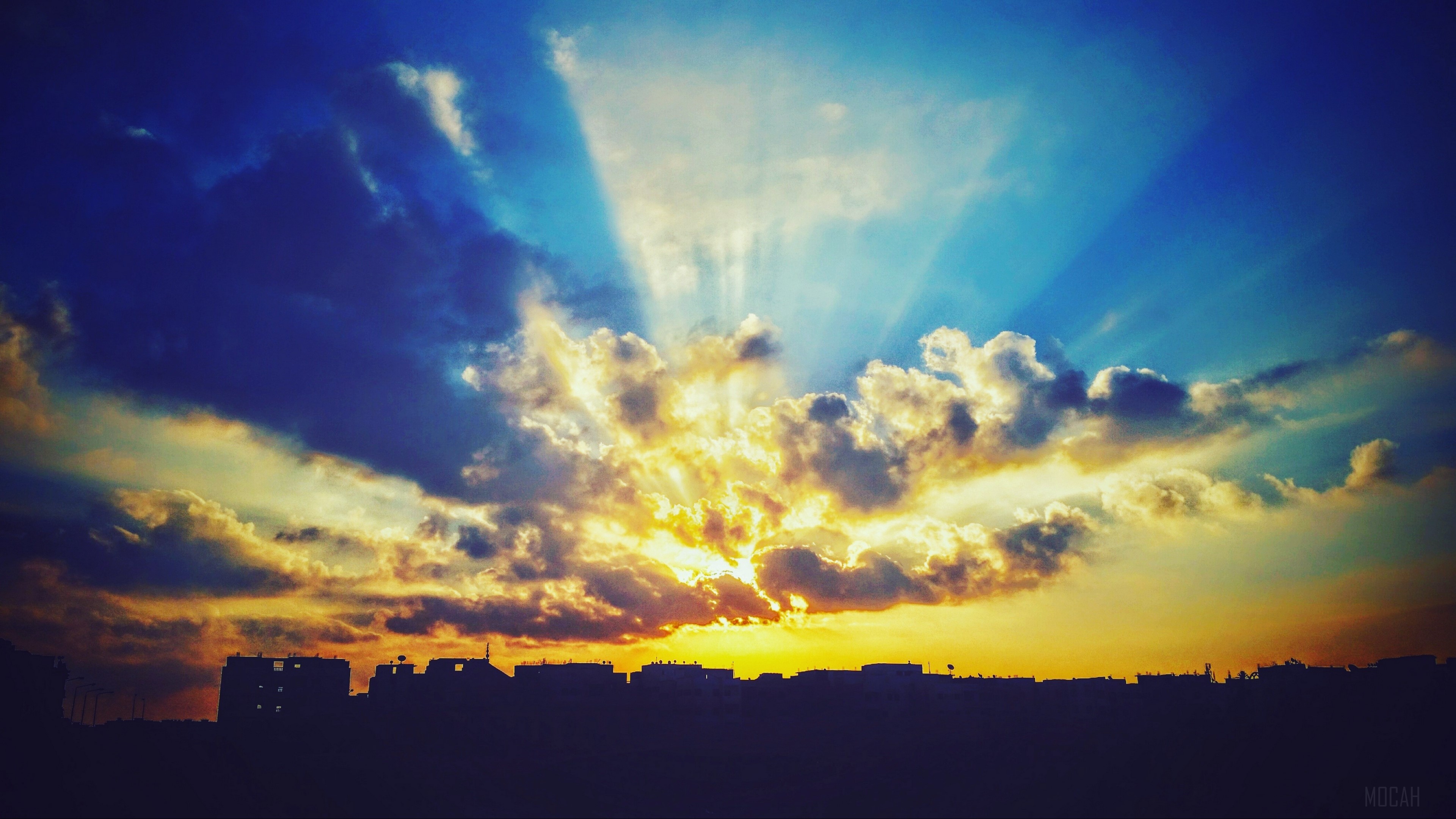 Sunset with crepuscular rays over city skyline HD Wallpaper