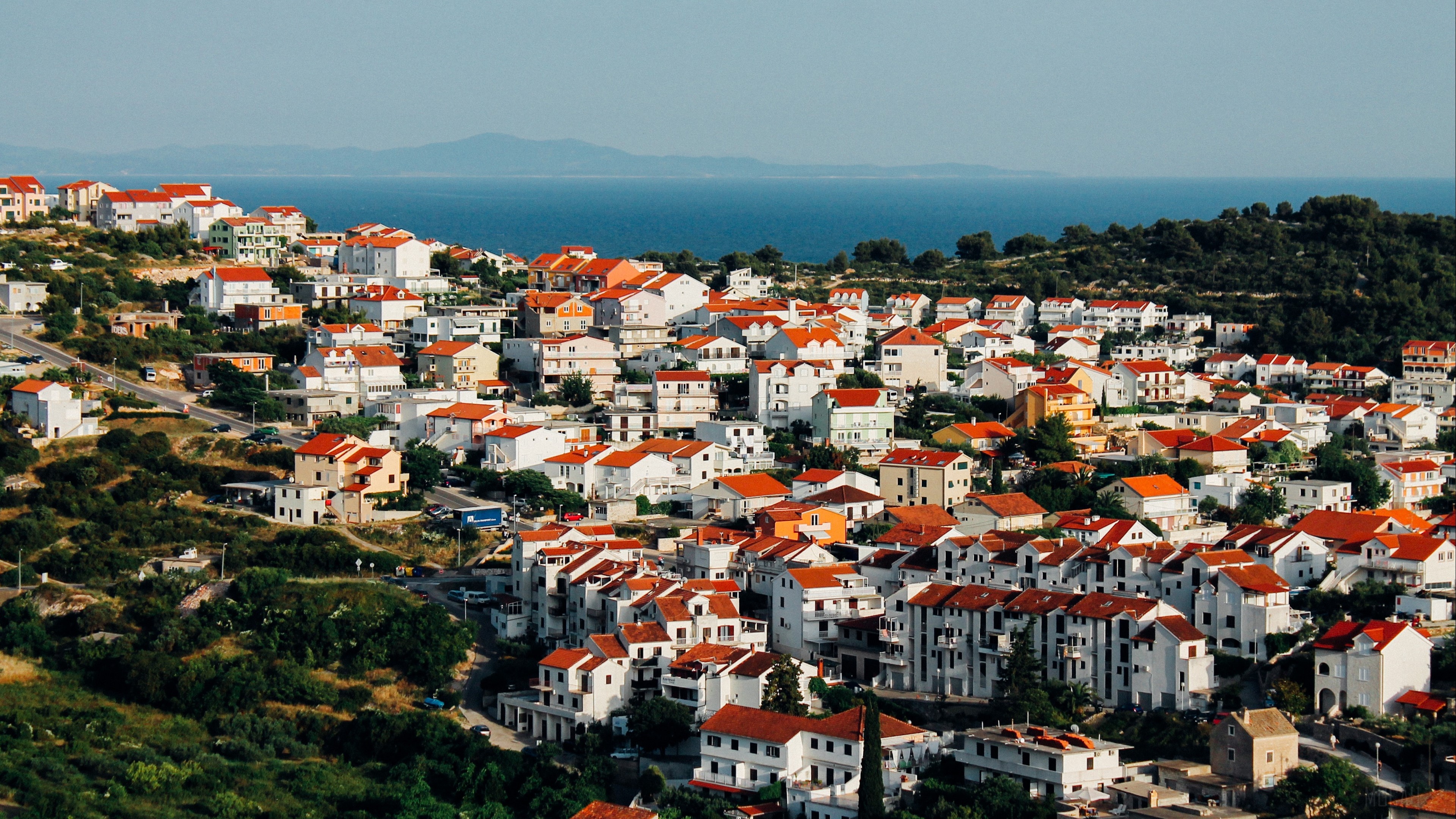 Cityscape with red-roofed buildings and the sea HD Wallpaper
