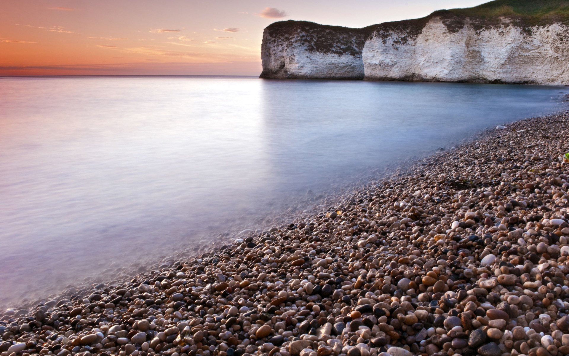Pebble beach with white cliffs and calm sea at sunset HD Wallpaper