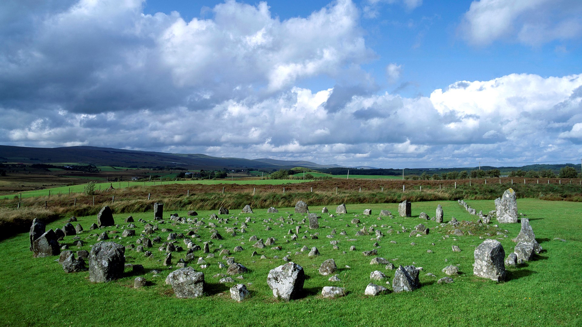 Standing stones in a grassy field under a cloudy sky HD Wallpaper
