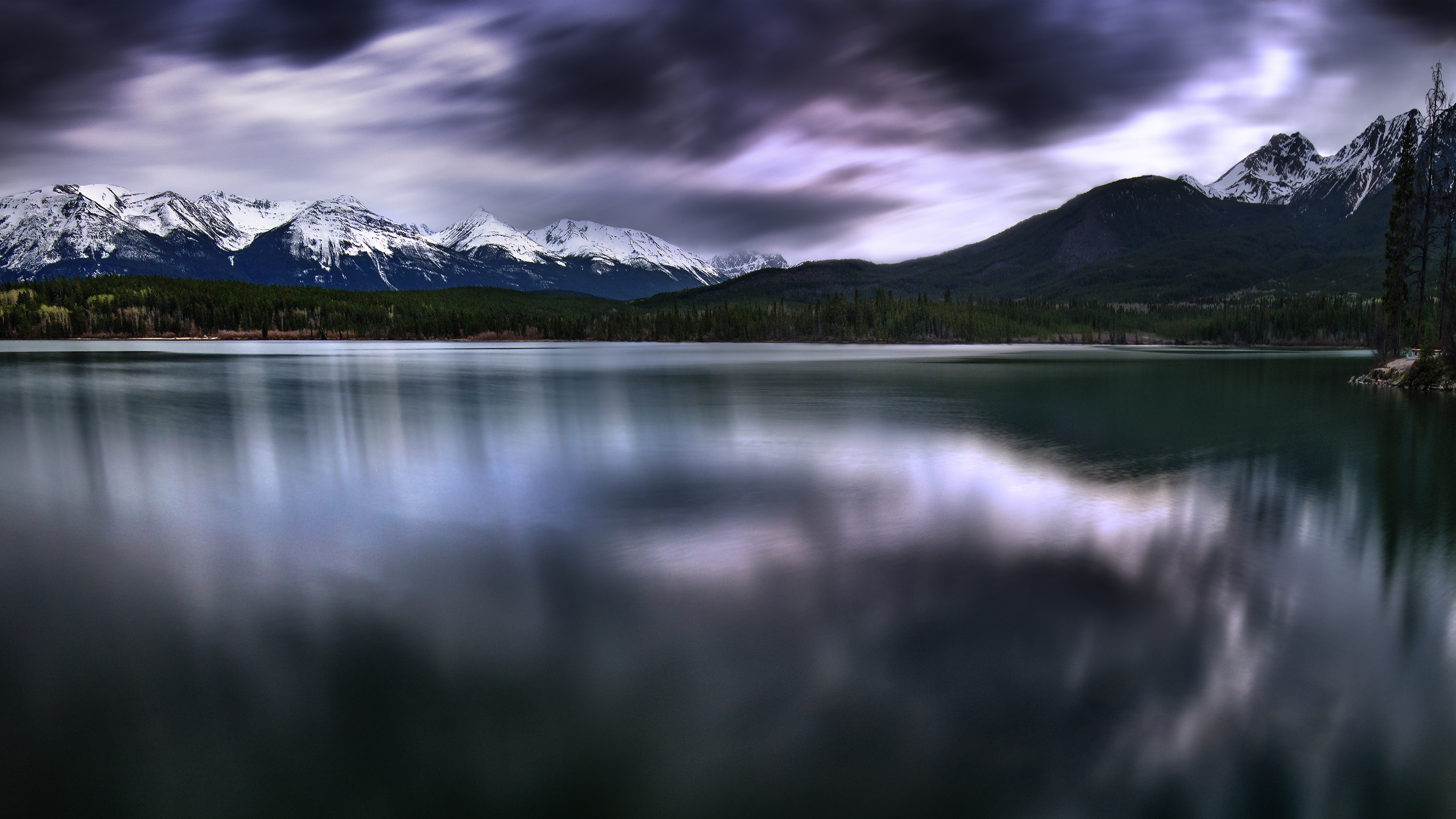 Snow-capped mountains reflected in a lake under a cloudy sky HD Wallpaper