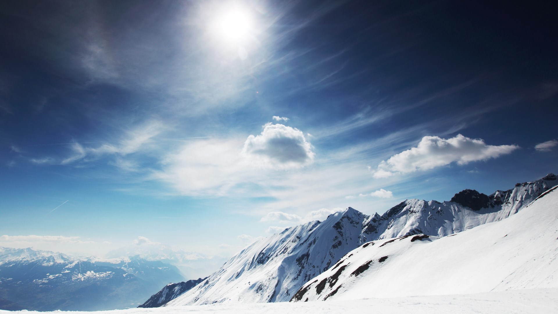 Snowy mountains under a bright sun and blue sky HD Wallpaper
