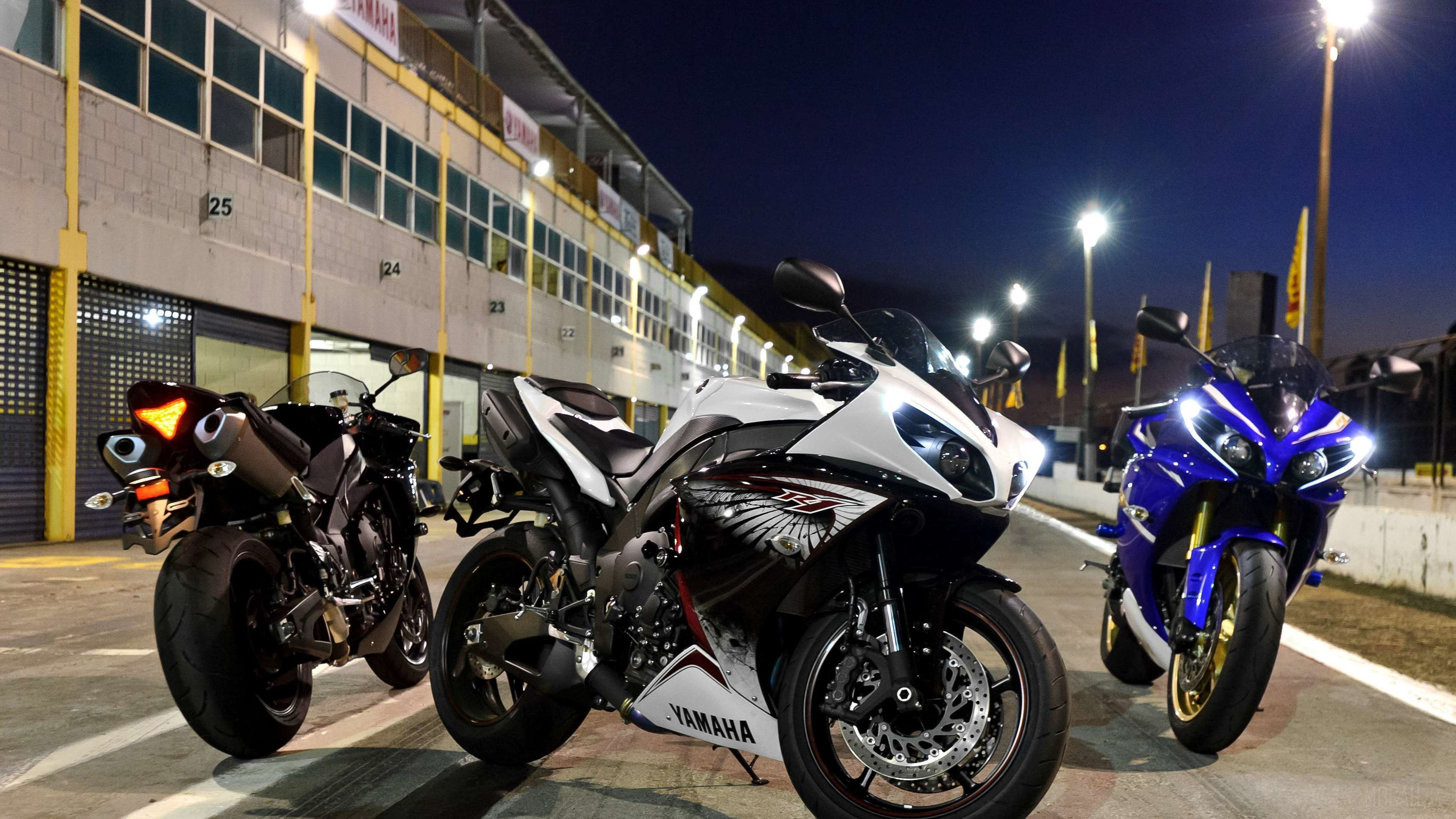 Three Yamaha R1 motorcycles on a race track at night HD Wallpaper