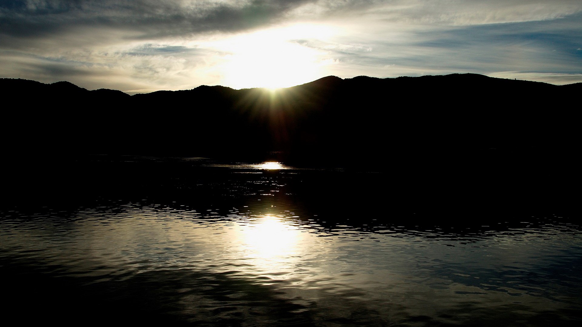 Sunset over a dark mountain range and water HD Wallpaper