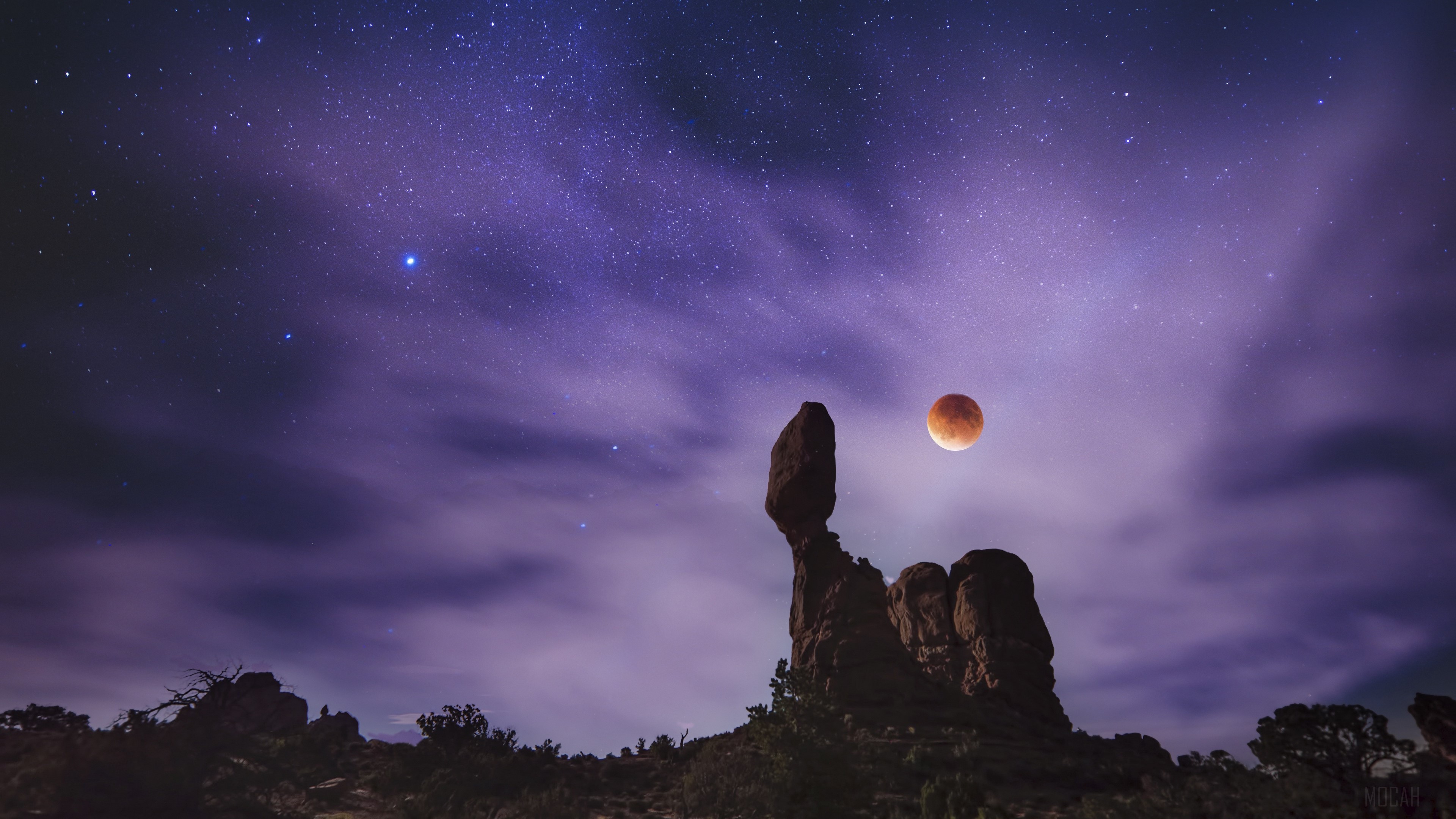 Lunar eclipse over rock formations under starry sky 4K HD Wallpaper